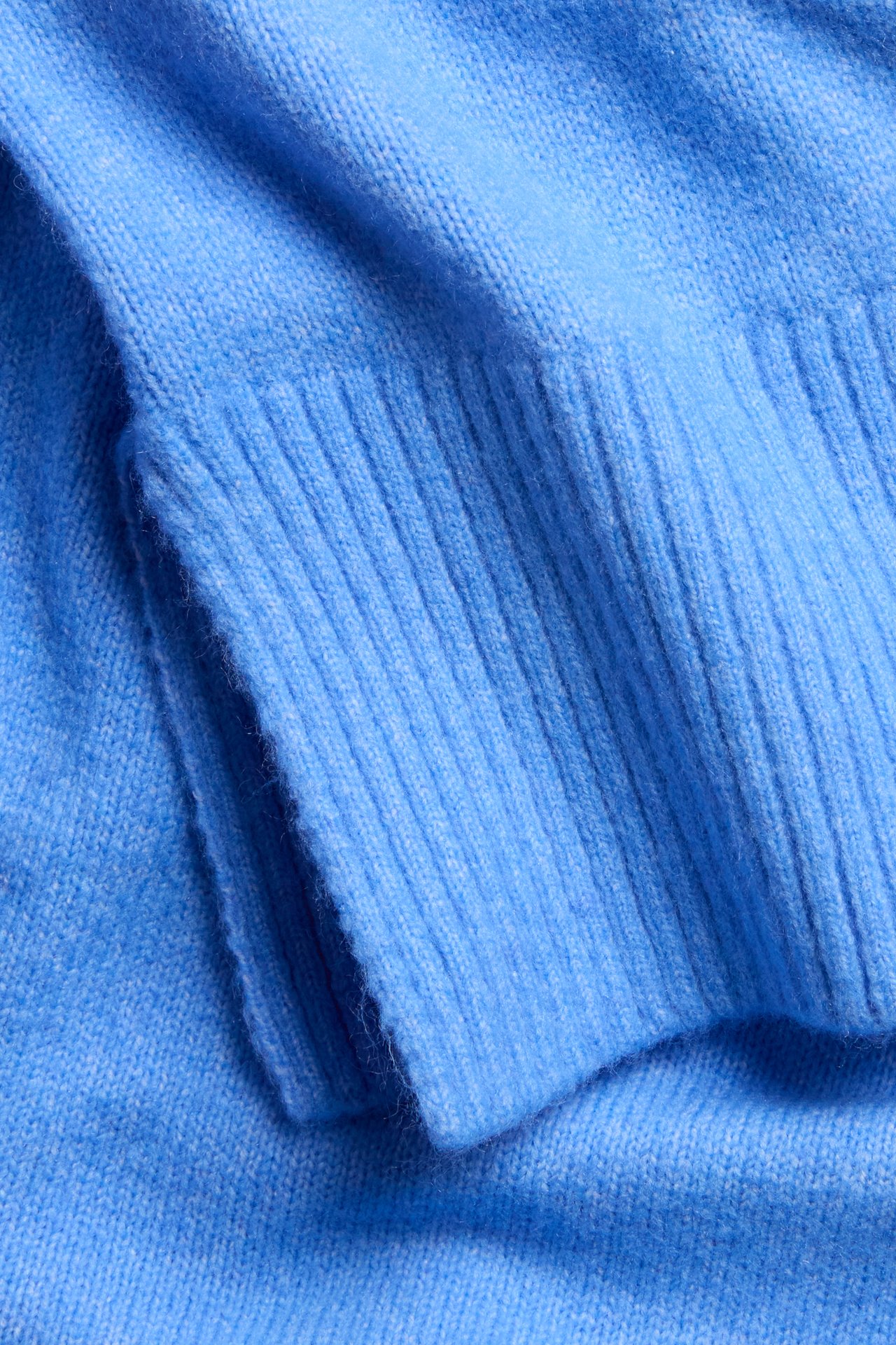 Nærbilde av en blå strikket pullover, som viser ribbestrikkede mansjetter og myk stofftekstur.