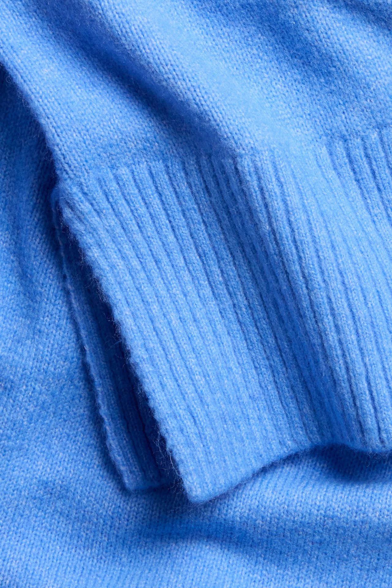 Nærbilde av en blå strikket pullover, som viser ribbestrikkede mansjetter og myk stofftekstur.