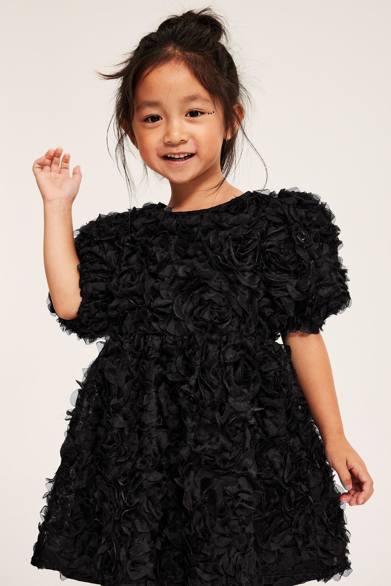 Widok z przodu dziecka w czarnej sukience z siateczki z 3D kwiatowym wzorem i bufiastymi rękawami.