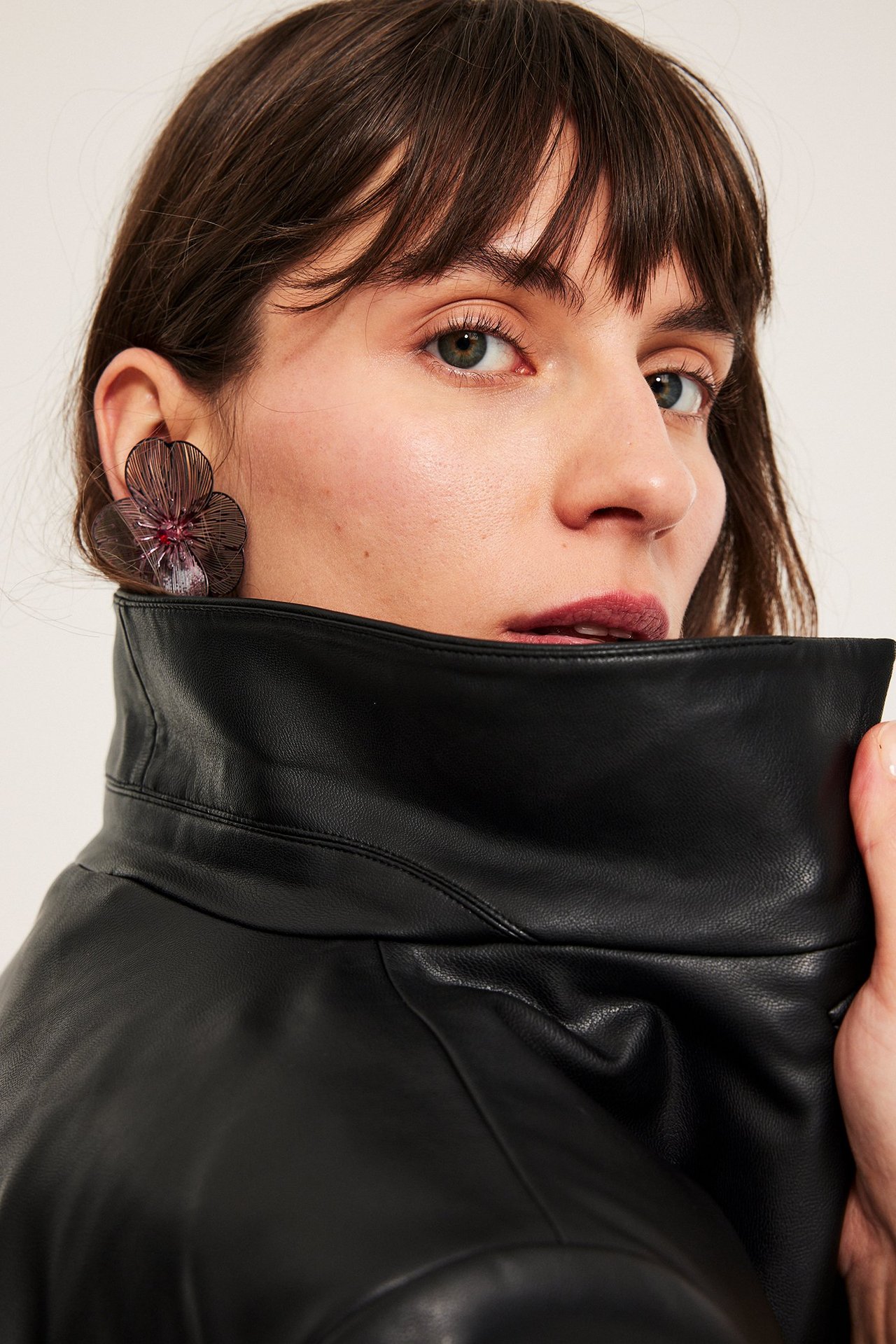 Zbliżenie kobiety z dużymi czerwonymi kwiatowymi kolczykami i czarną skórzaną kurtką, z boku.