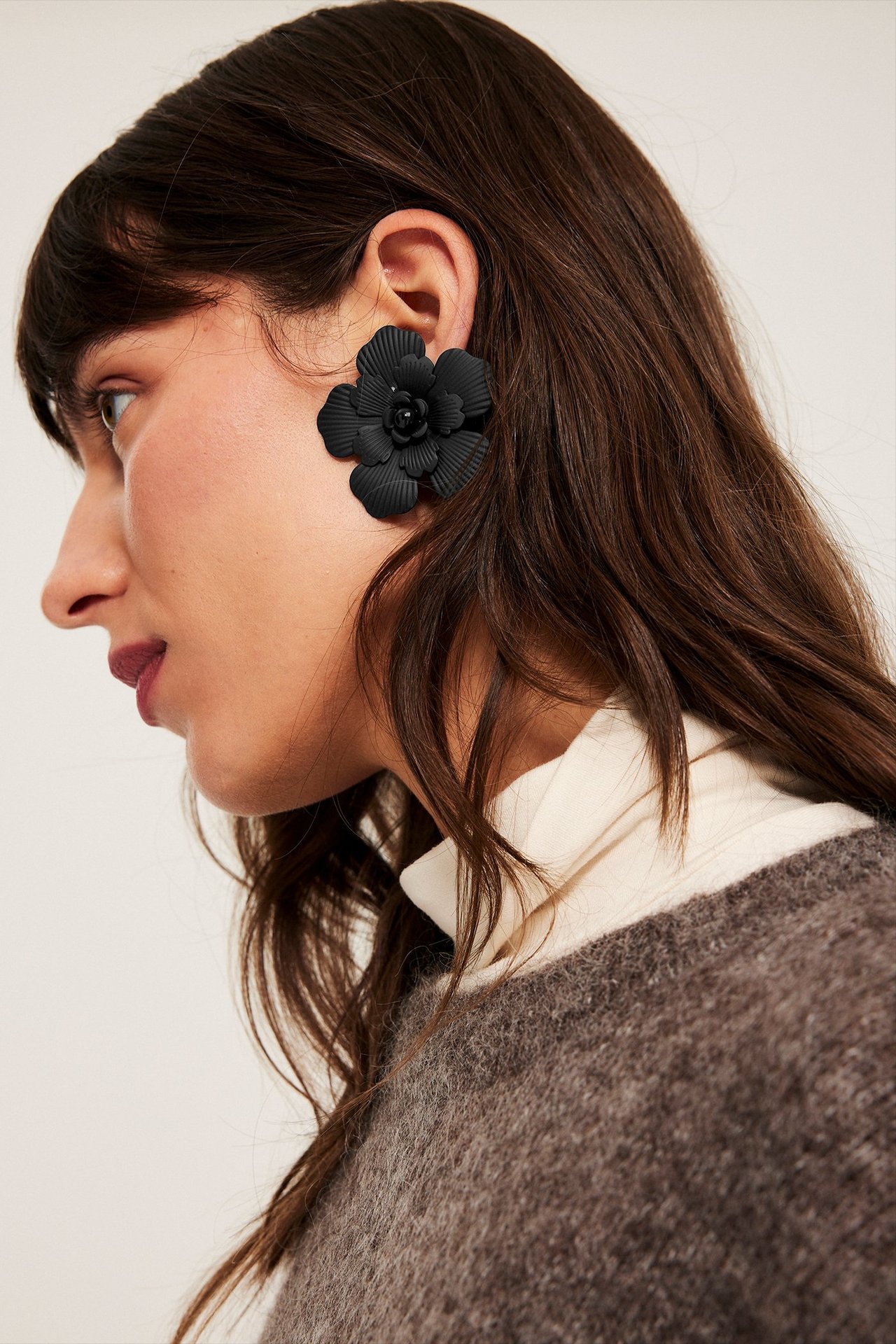 Suuret mustat kukkakorvakorut lasista, keskitytään naisen vasempaan korvaan.