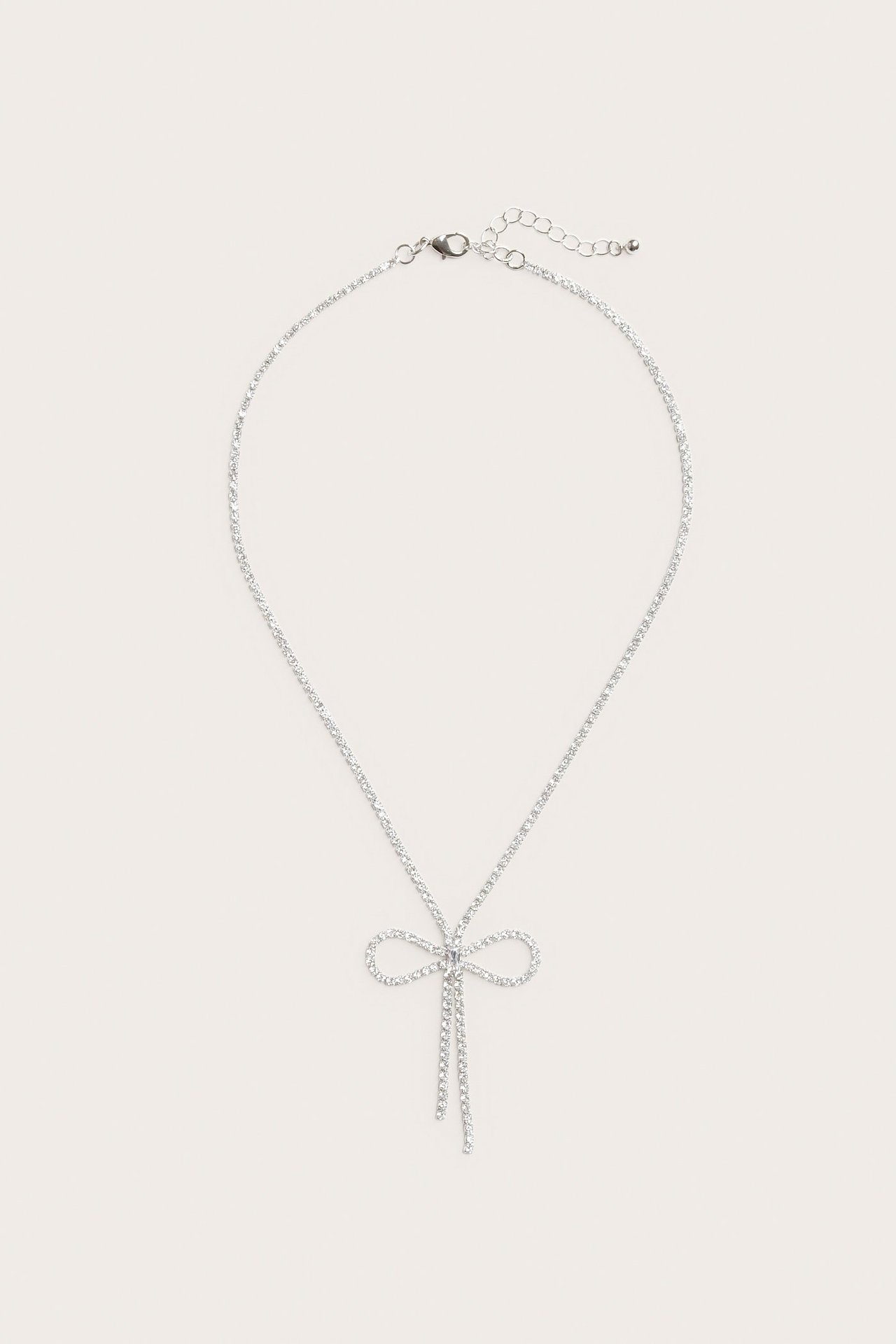 Framsida av ett silverfärgat strasshalsband med rosettformat hänge och karbinlås.