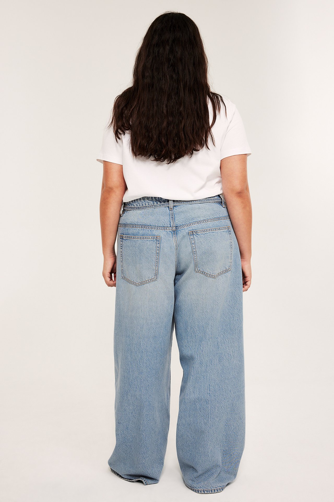Bakfra: kvinne i lyseblå høy midje, vide jeans med lommer og en hvit t-skjorte.