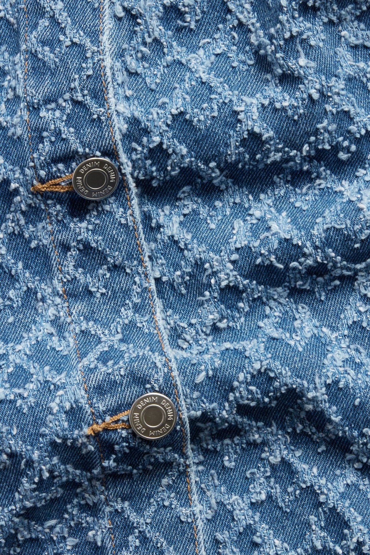 Zbliżenie na niebieską dżinsową sukienkę z fakturowanym wzorem w serca i srebrnymi guzikami 'DENIM'.