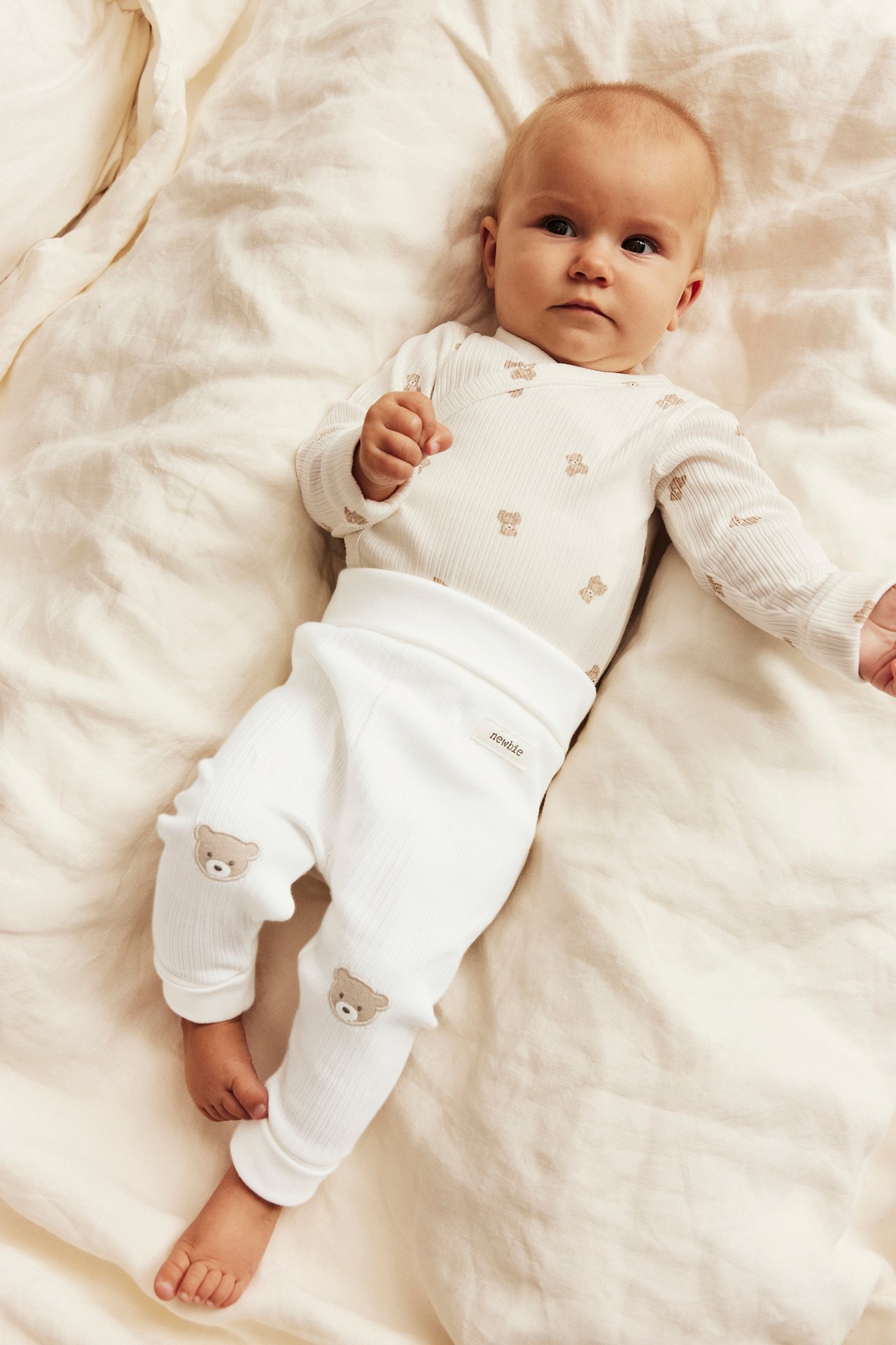 Baby i hvit ribbet body med bamsemønster og matchende bukse med bamser på knærne.
