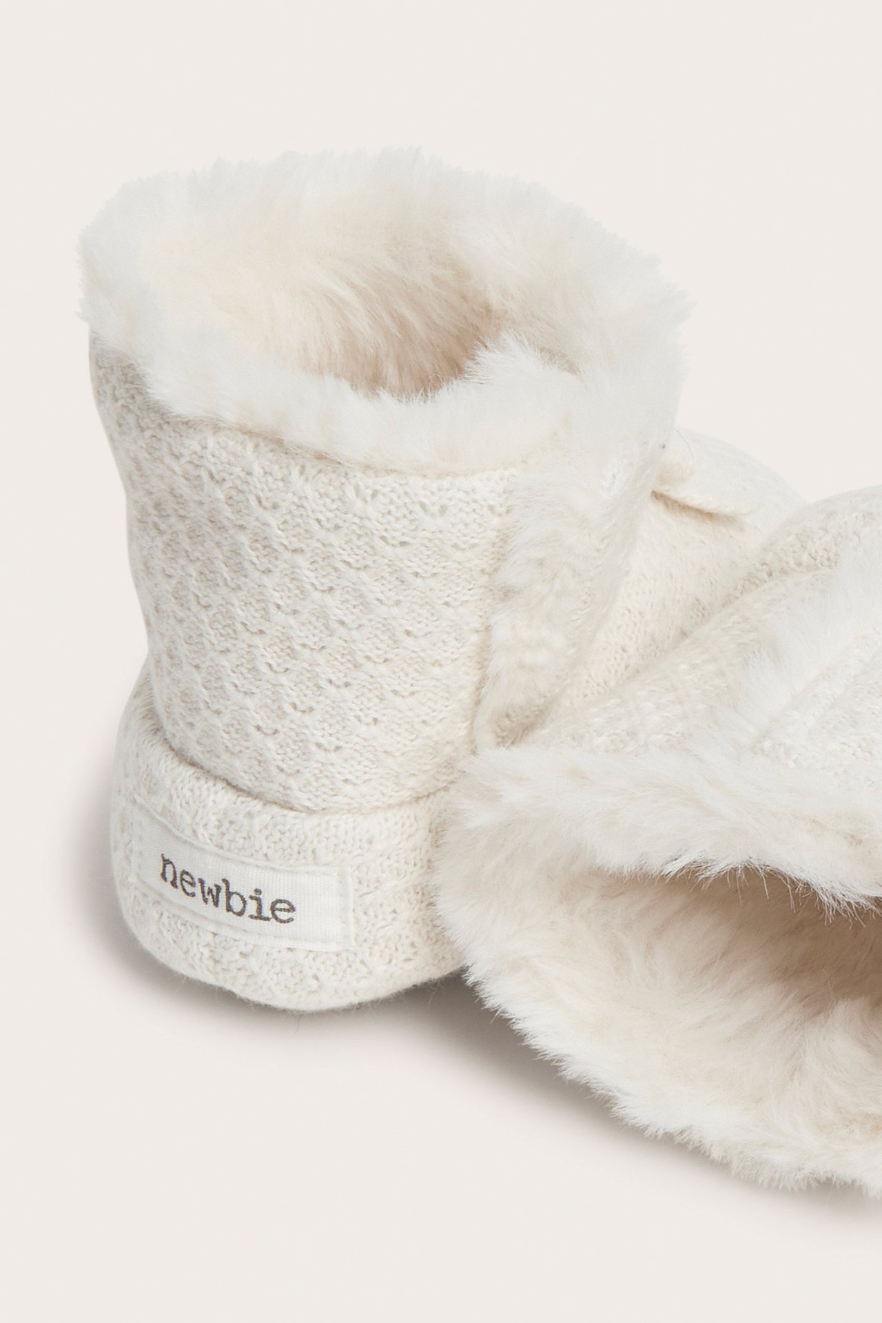Zbliżenie na kremowe dzianinowe buciki niemowlęce z teksturowanym wzorem, futerkową podszewką i zapięciem na rzep.