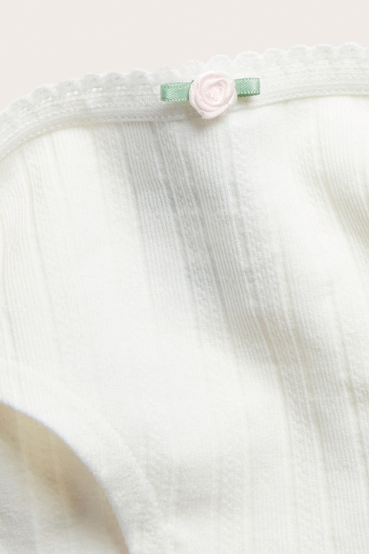 Zbliżenie: off-white bezszwowe figi z fakturą pointelle, mała różowa kokardka w talii.