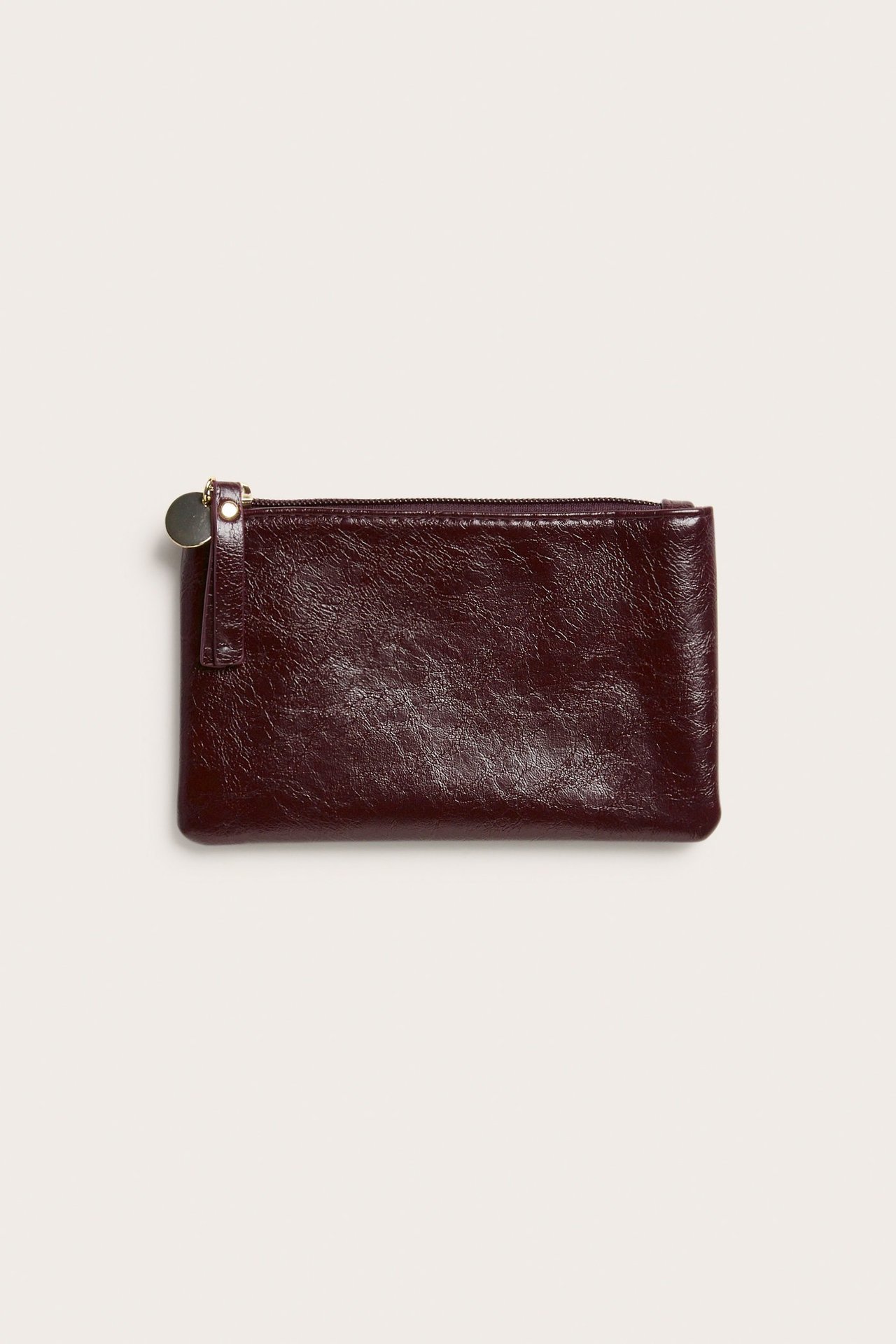 Widok z przodu małej, bordowej torebki z teksturą, zamkiem błyskawicznym i złotą zawieszką.