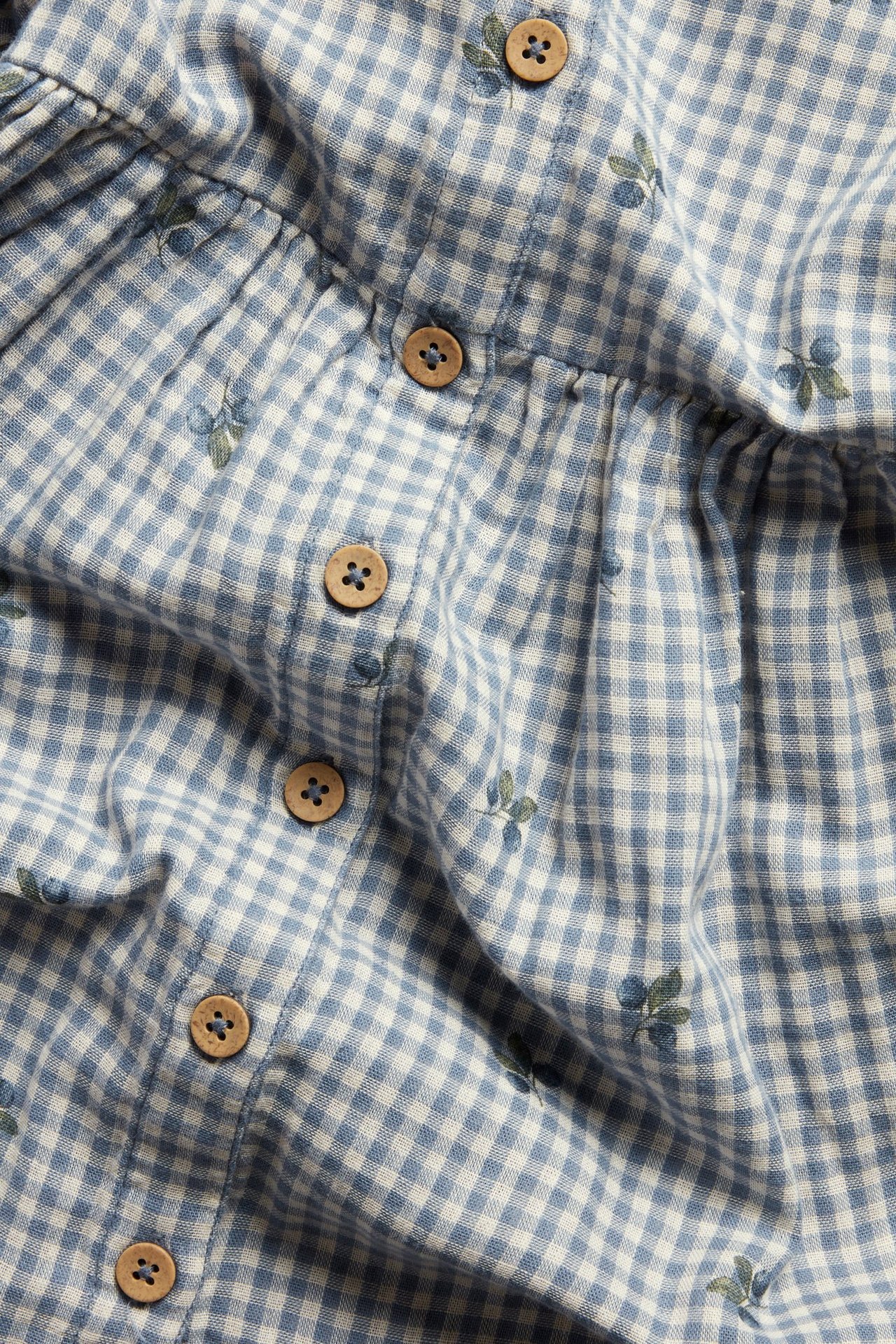 Zbliżenie niebiesko-białej sukienki w kratę z jagodami i widocznymi drewnianymi guzikami.