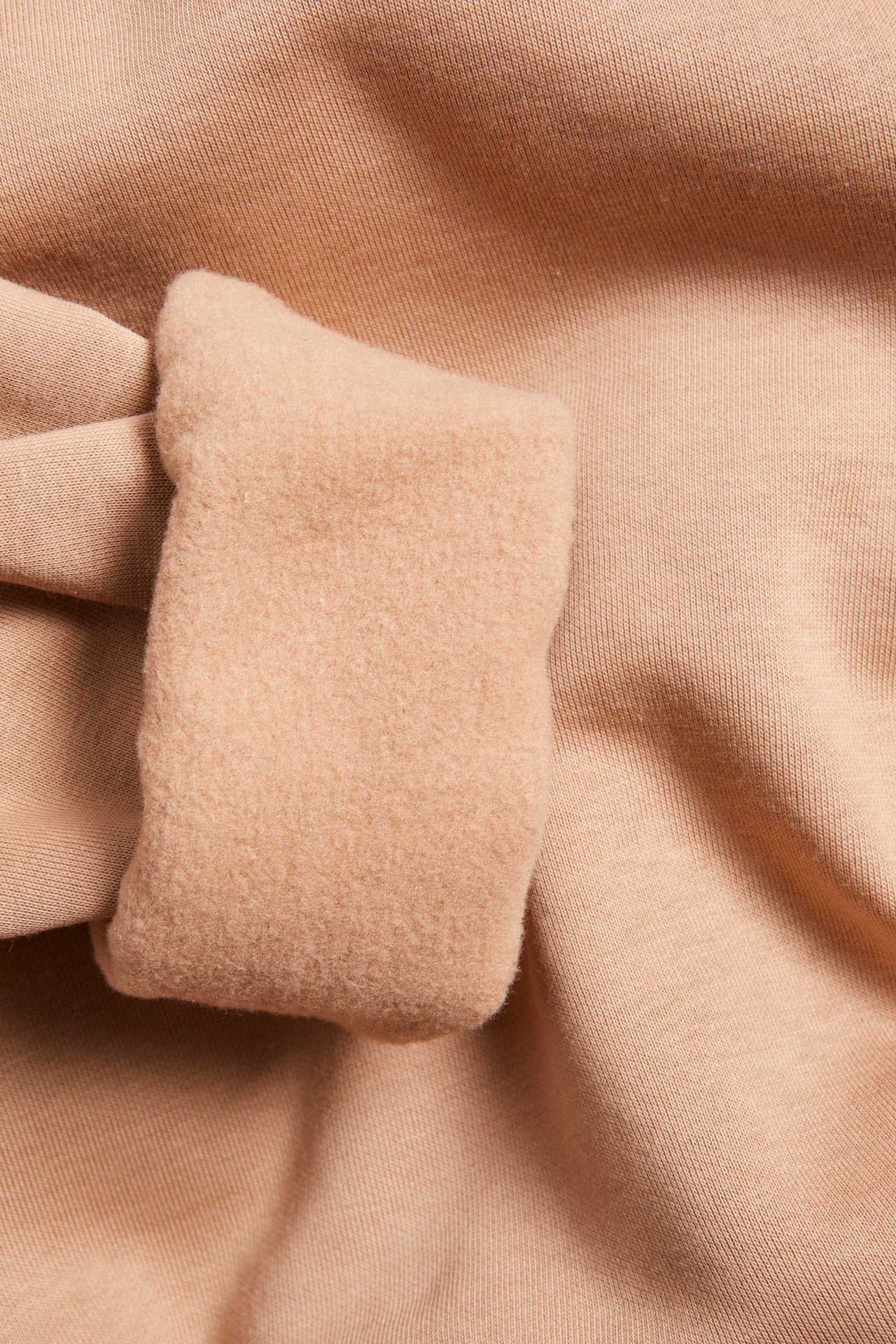 Nærbilde av en beige bomullsblanding-sweatshirt, som viser en tykkere, børstet mansjett.