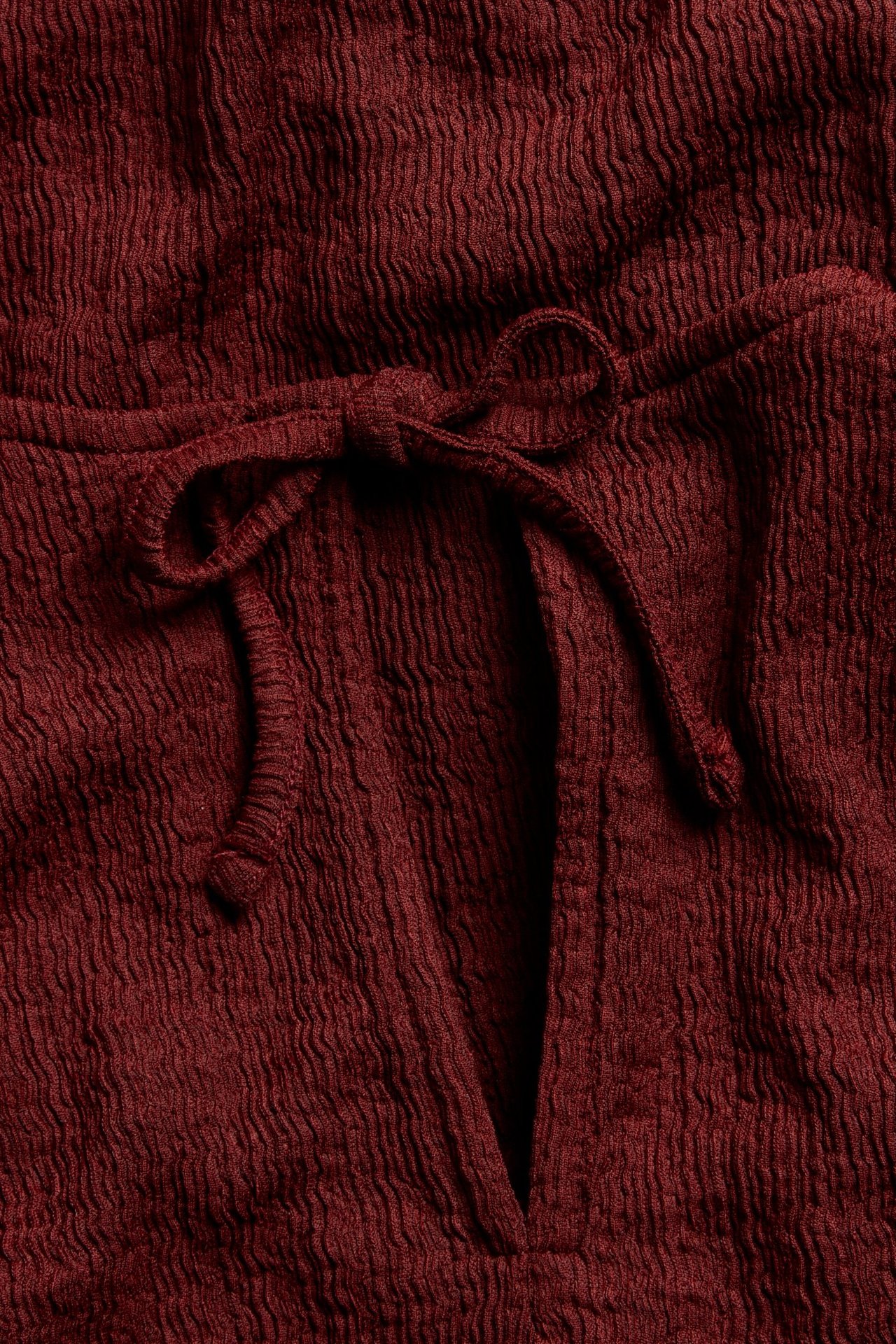 Zbliżenie czerwonego teksturowanego topu z dekoltem w serek i wiązaną kokardą.