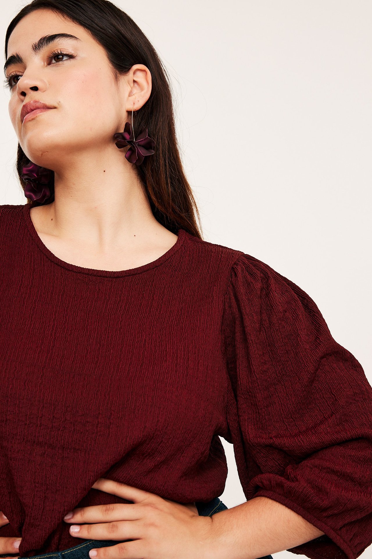 Zbliżenie z przodu: kobieta w czerwonym teksturowanym topie z bufiastymi rękawami i ciemnofioletowymi kolczykami-kwiatami.