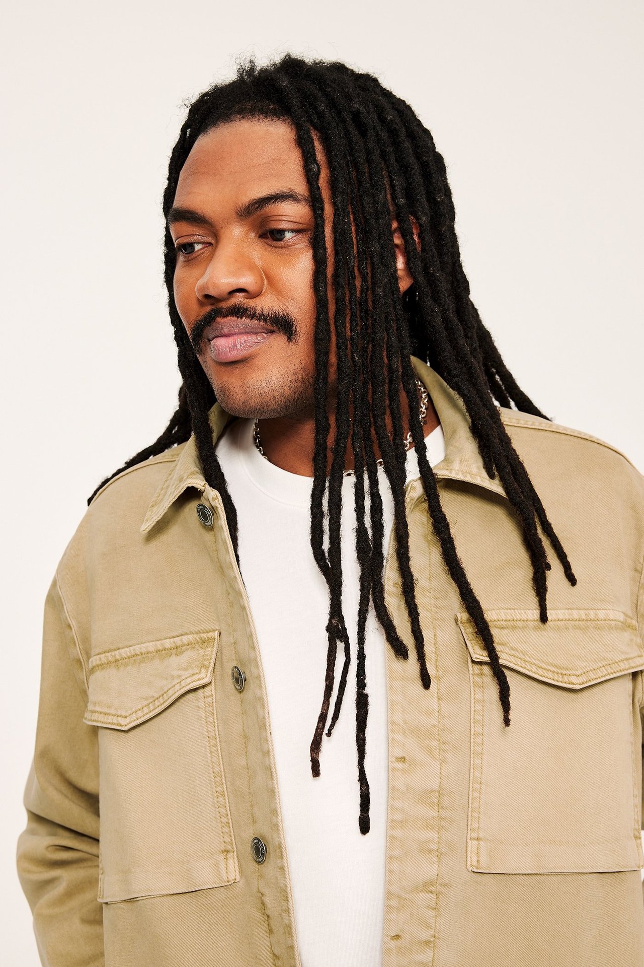 Widok z przodu: mężczyzna w beżowej kurtce z twillu bawełnianego z dużymi kieszeniami, na białym t-shircie.