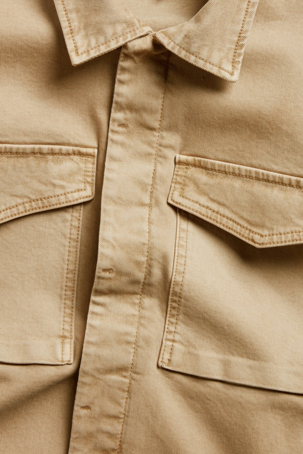 Zbliżenie beżowej kurtki z diagonalu bawełnianego z guzikami i dwoma dużymi kieszeniami z klapami.
