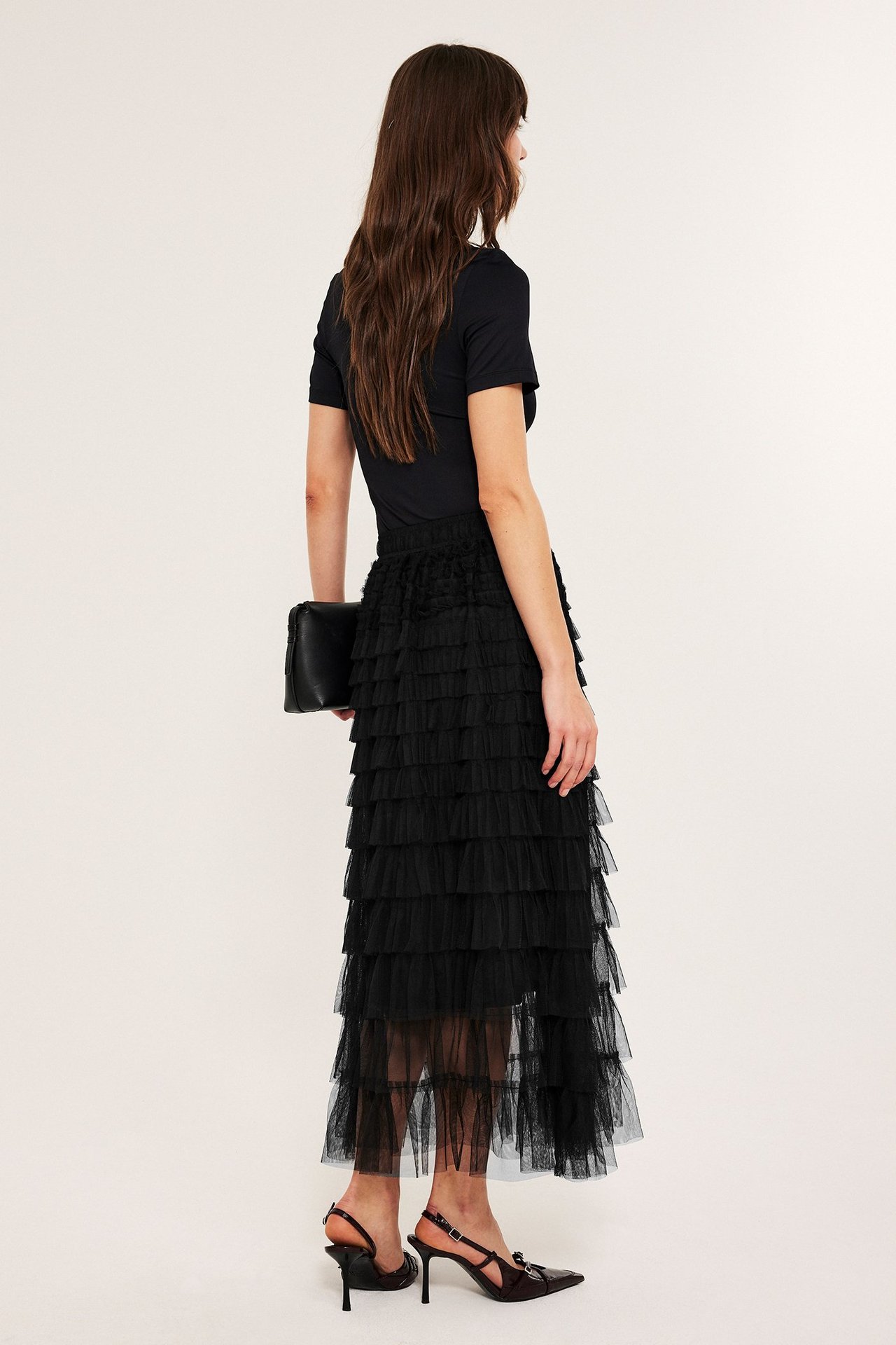 Kobieta w długiej czarnej spódnicy z tiulowymi frędzlami, elastyczna talia, bok widok.