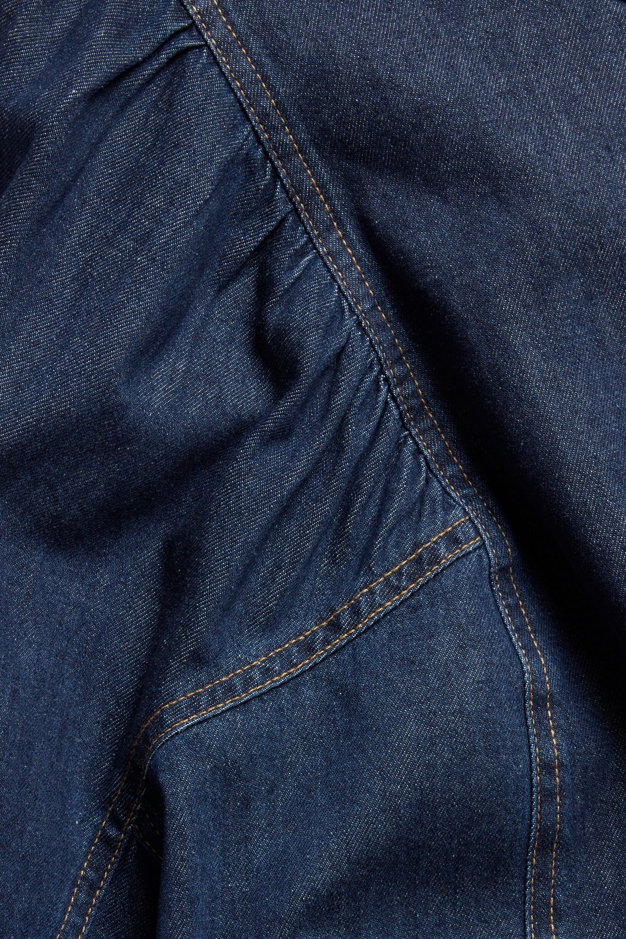 Zbliżenie na ciemnoniebieski materiał dżinsowej bluzki z kontrastowymi przeszyciami i marszczonymi detalami.