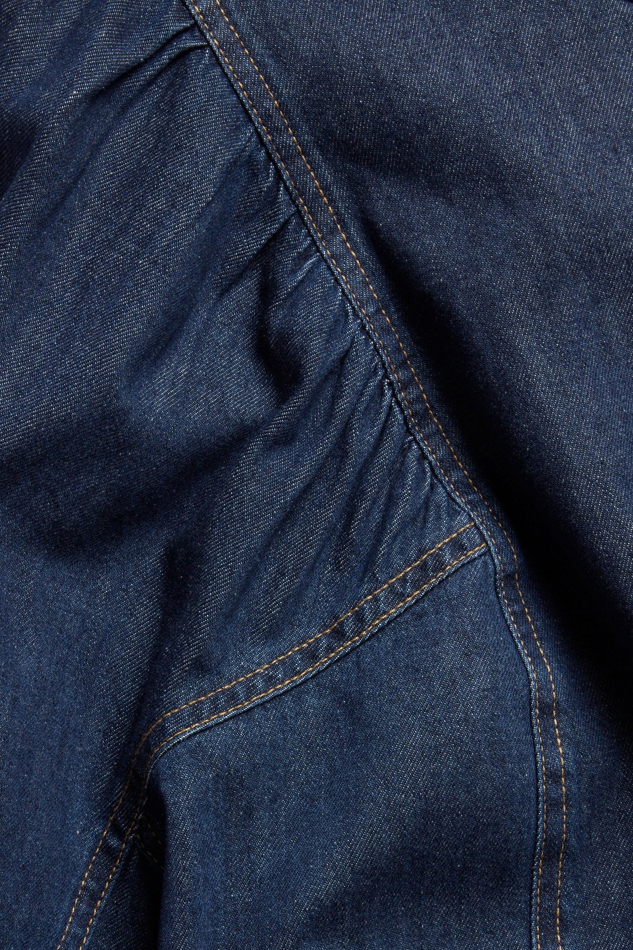 Närbild på mörkblått denimblustyg med kontrasterande stickningar och rynkade detaljer.