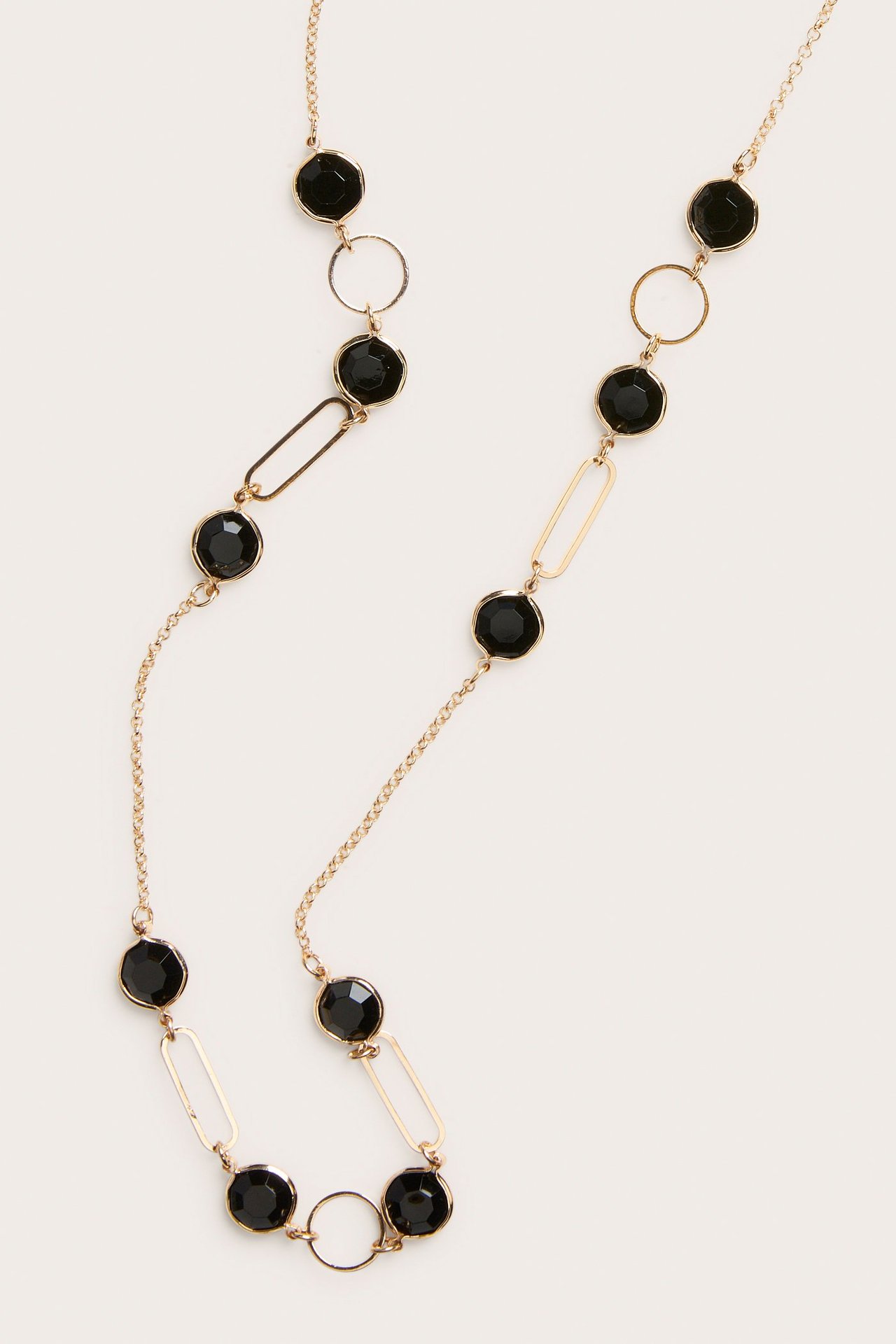 Närbild av guldfärgat halsband med svarta glasdetaljer, ovala länkar och runda ringar.