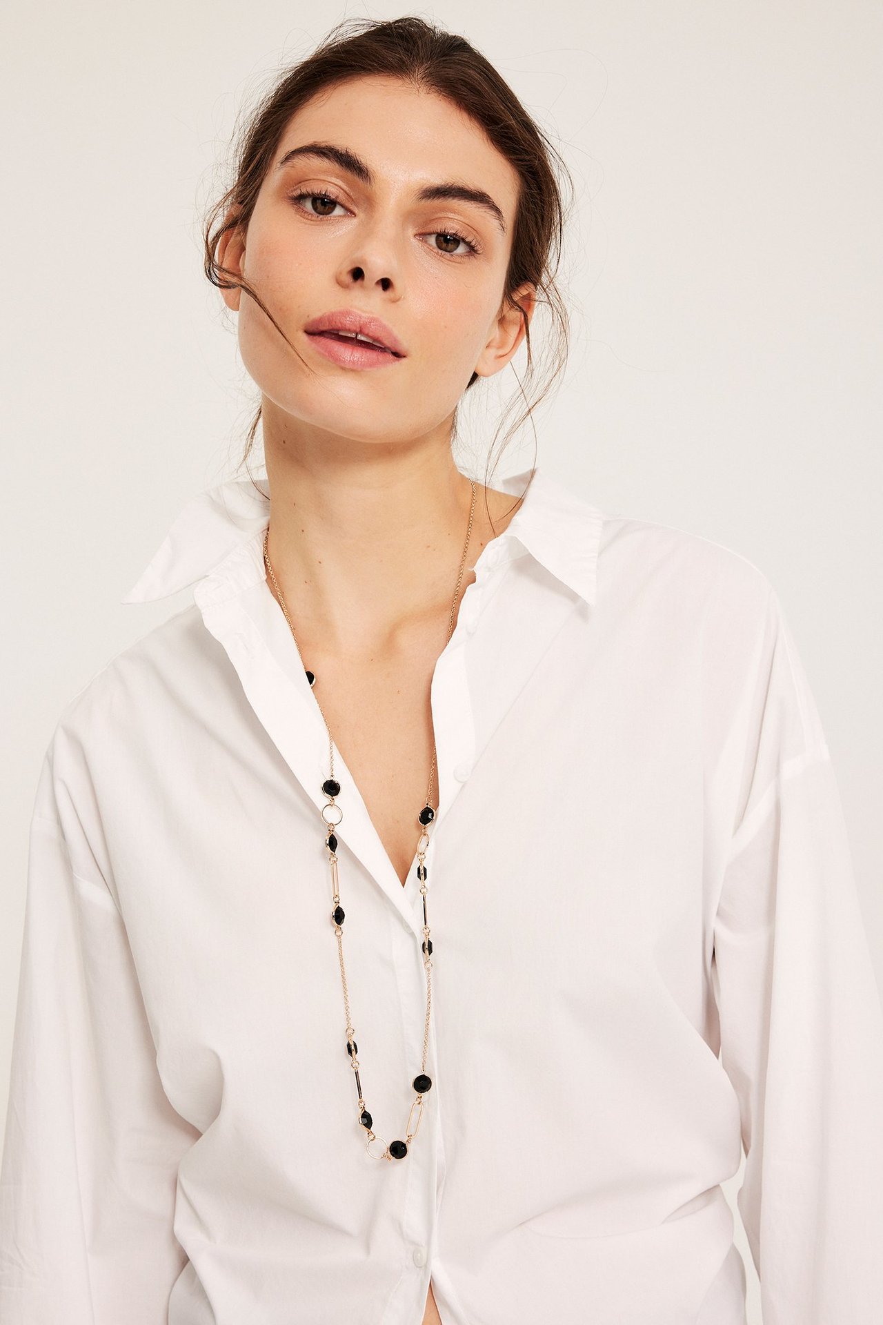 Zbliżenie kobiety noszącej złoty naszyjnik z czarnymi szklanymi detalami na białej koszuli.