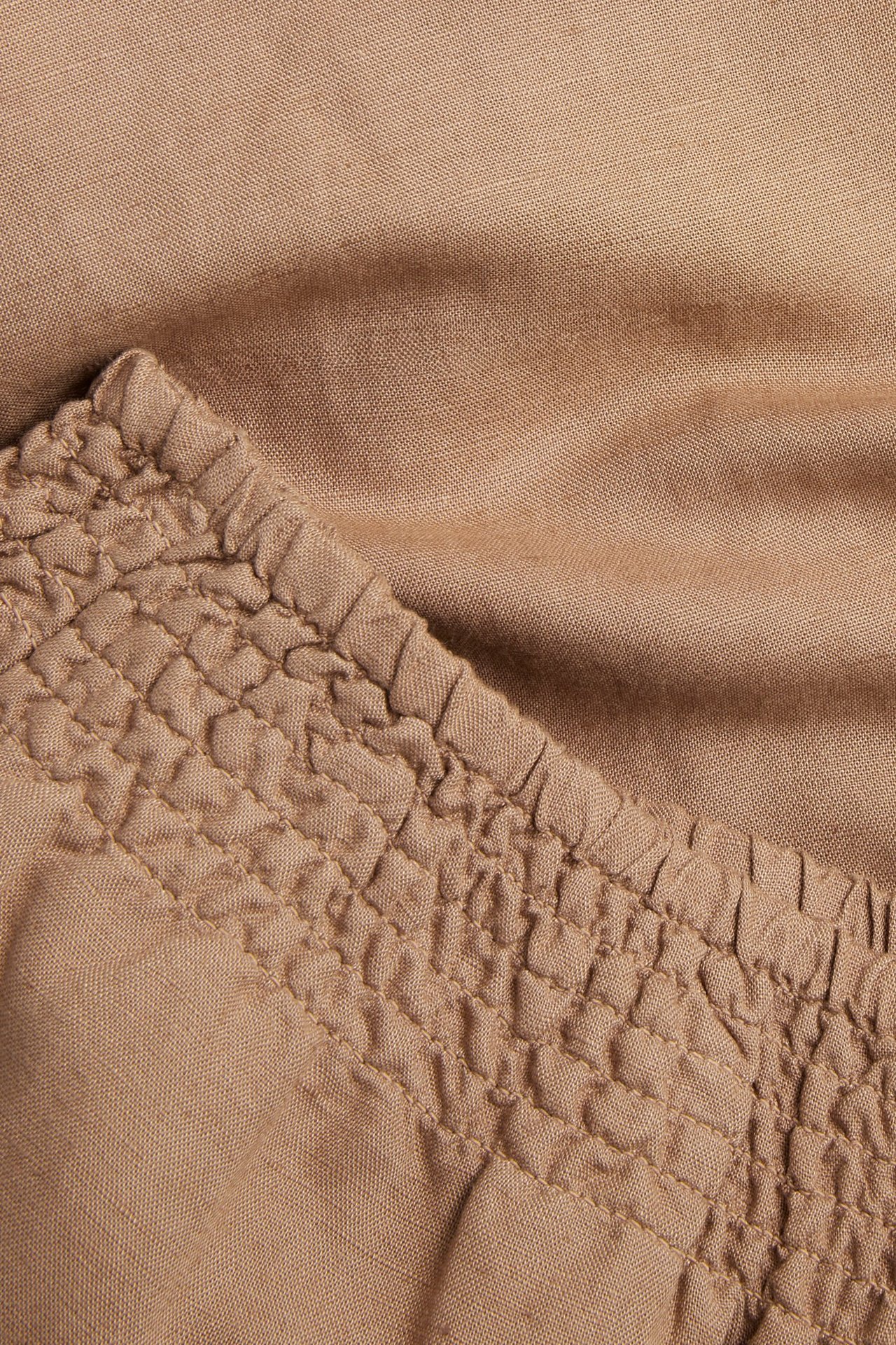 Zbliżenie na beżowe spodnie z mieszanki lnu ze ściągaczem z marszczeniem.