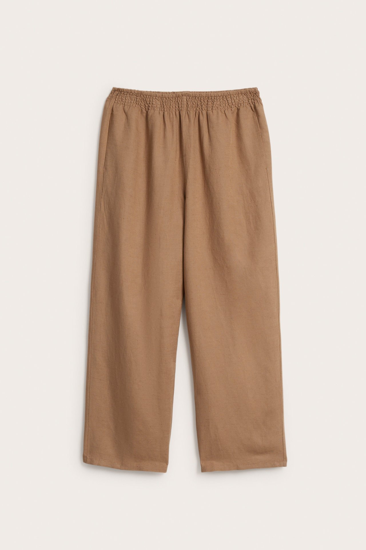 Frontvy av beiga byxor i linnemix med smockresår i midjan och vida ben.