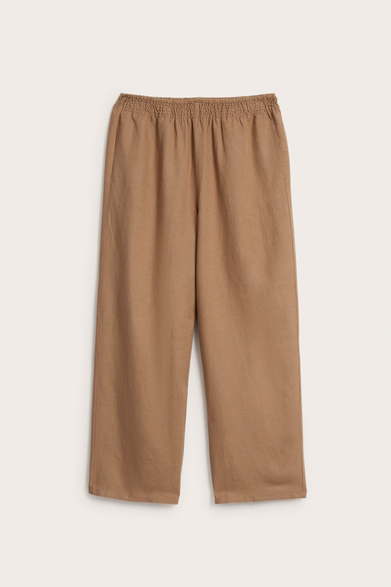 Frontvy av beiga byxor i linnemix med smockresår i midjan och vida ben.