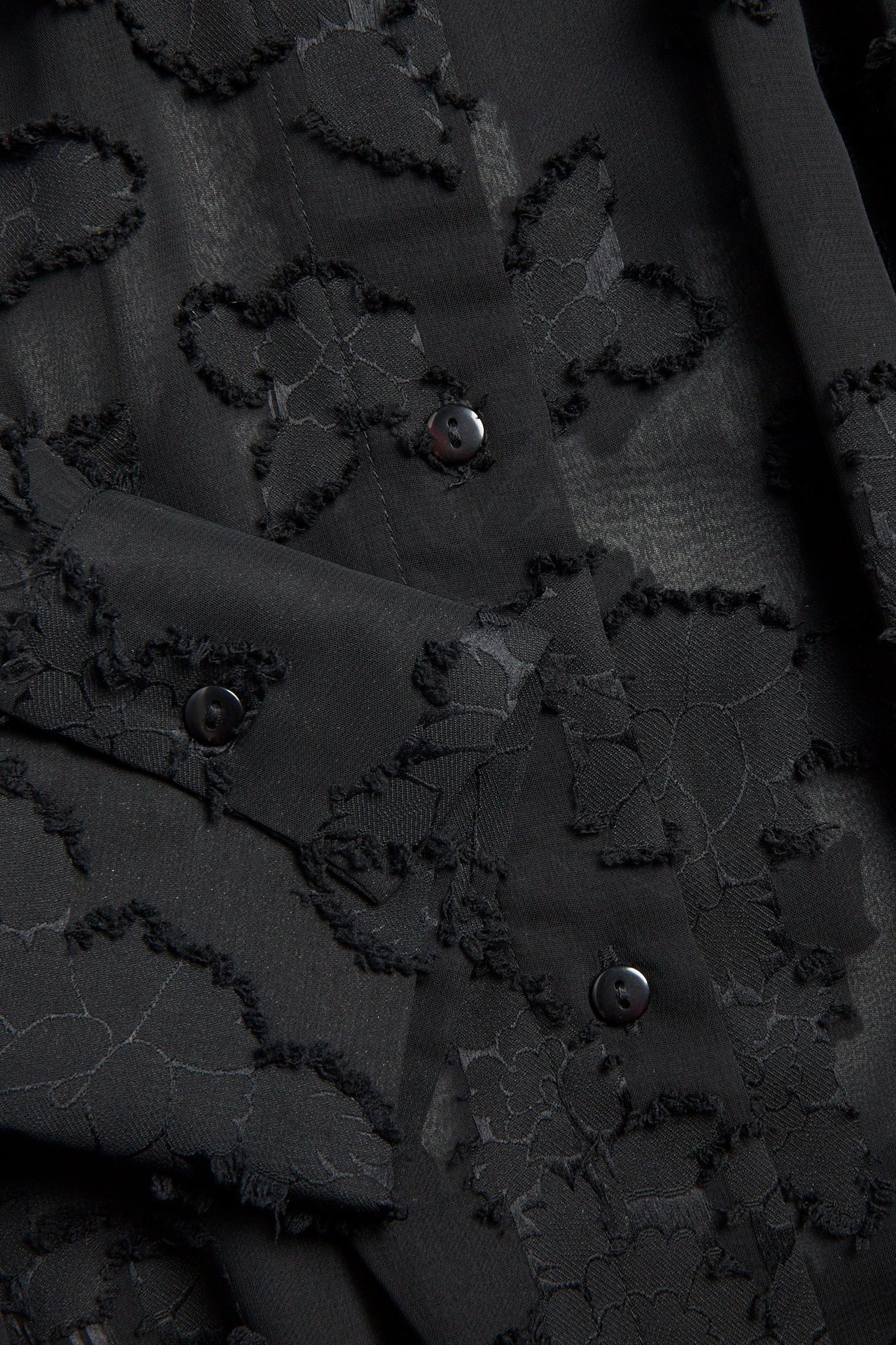 Zbliżenie czarnej koszuli z żakardu krepowego z teksturowanym kwiatowym wzorem i ciemnymi guzikami.