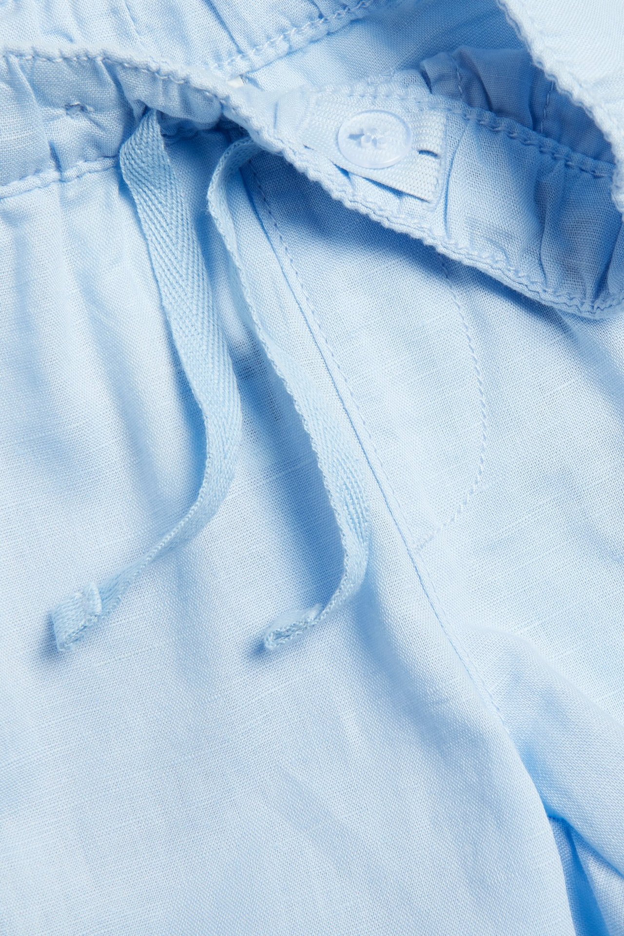 Lähikuva lasten vaaleansinisistä pellavasekoiteshortseista, joissa on kiristysnyöri ja säädettävä nappivyötärö.