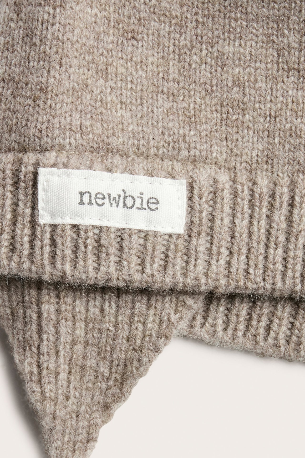 Zbliżenie na melanżową brązową wełnianą czapkę niemowlęcą z nausznikami i białą metką.
