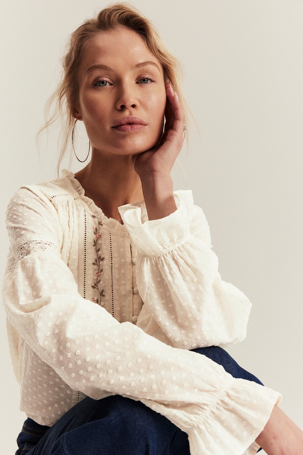 Edestä: Nainen yllään luonnonvalkoinen puuvillapusero kukkakirjonnalla, pitsillä, röyhelökauluksella ja -hihansuilla. Yllään tummat farkut.