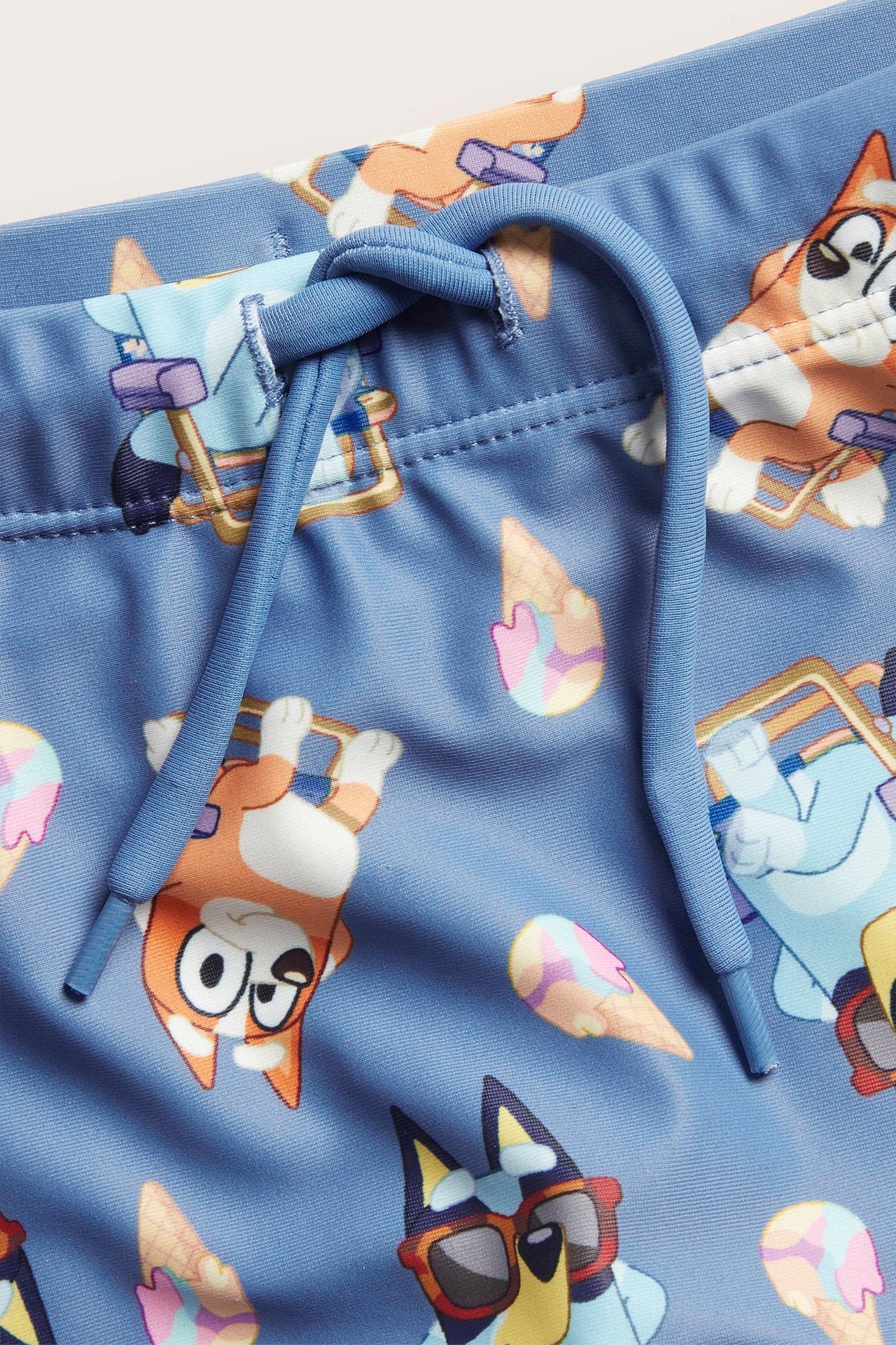 Lähikuva edestä: siniset lasten Bluey-kuvioidut uimashortsit solmitulla kiristysnyörillä.