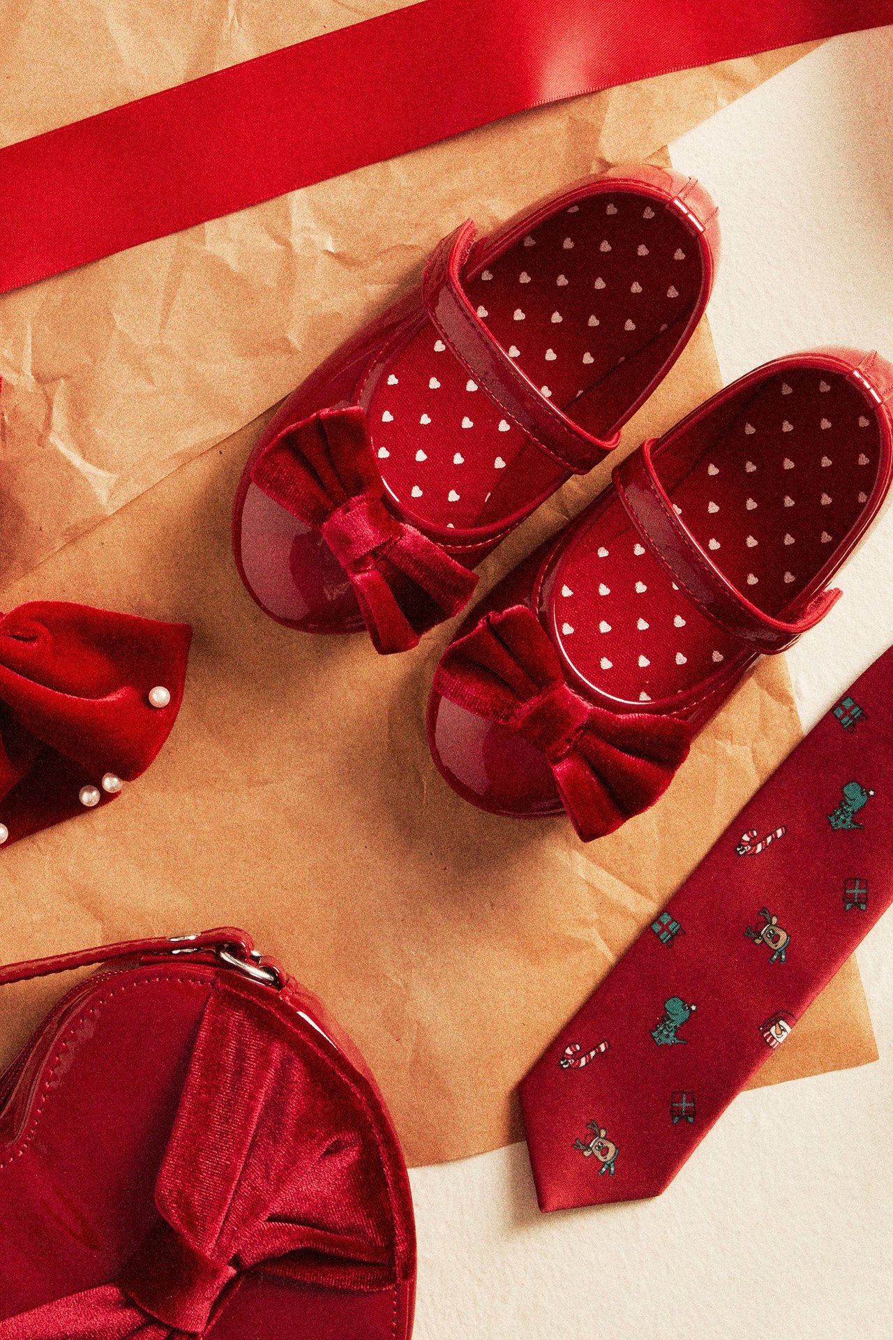 Ylhäältä kuvatut punaiset kiiltonahkaiset ballerinakengät samettinauhoilla, sydänpohjallisilla, pannan ja solmion vieressä.
