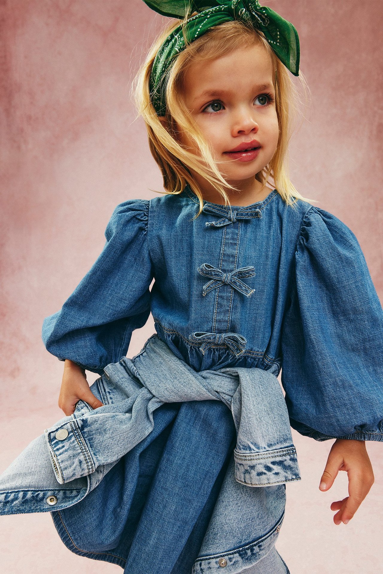 Edestä: Lapsi vaaleassa farkkumekossa ruseteilla, pussihihoilla, farkkutakki vyötäröllä, vihreä huivi.