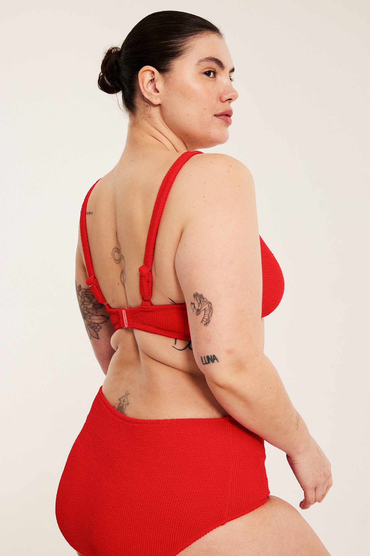 Bakifrån: kvinna i röd strukturerad bikinitopp med justerbara axelband och knäppe, samt matchande trosa.