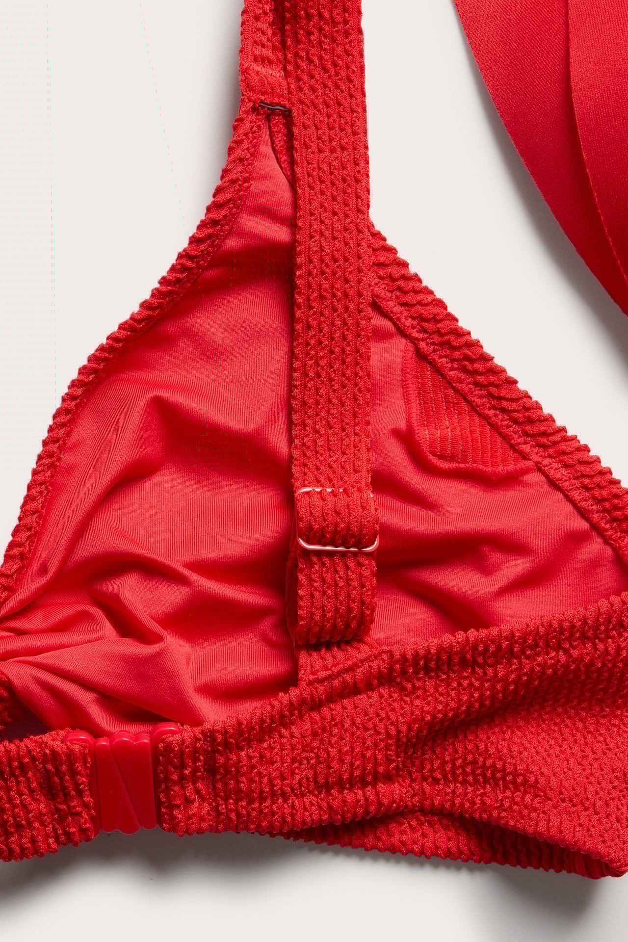 Närbild av en röd strukturerad bikini-bh med justerbara axelband och knäppe i ryggen.