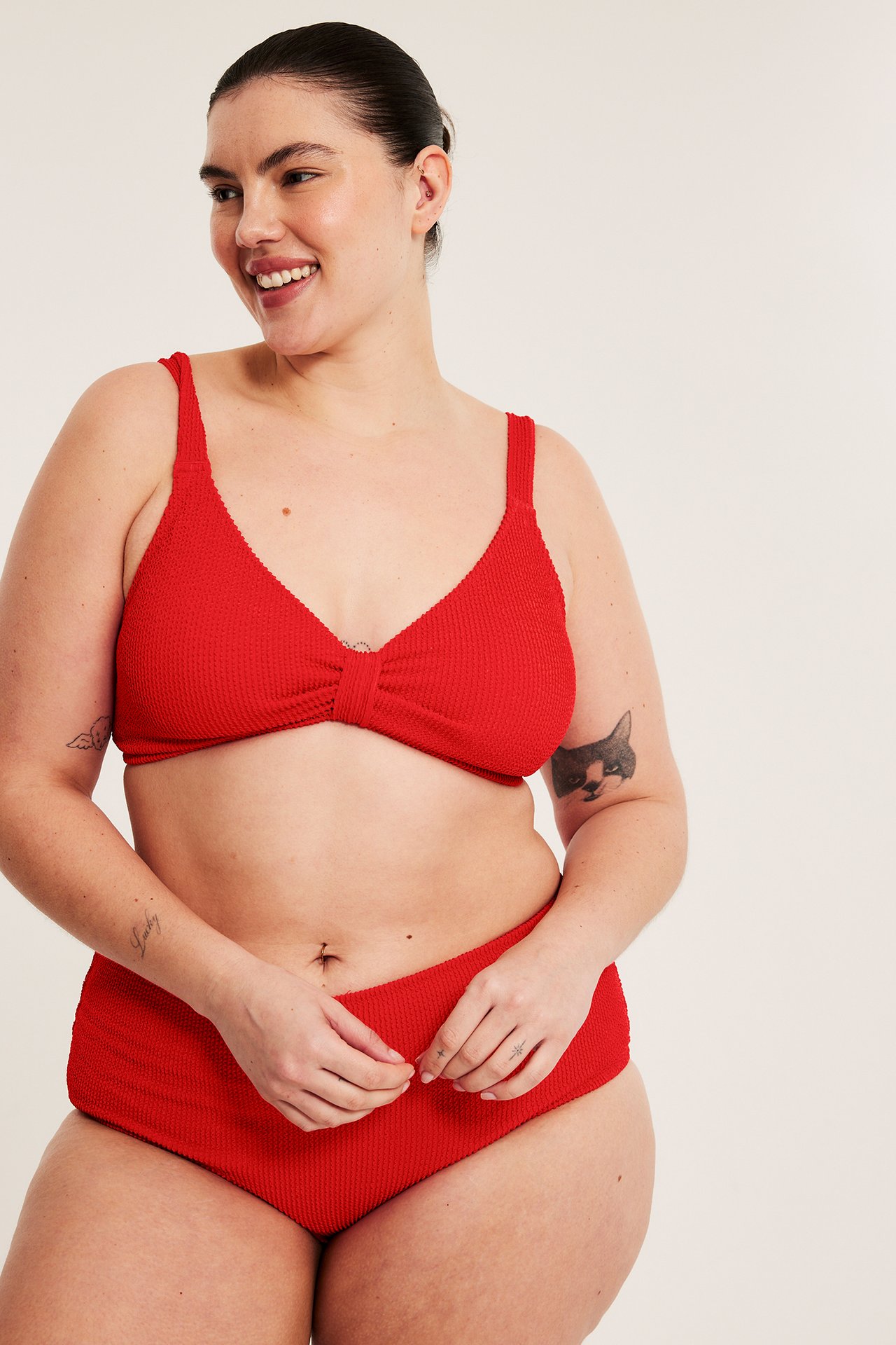 Framifrån: Kvinna i röd strukturerad bikini-bh med knytdetalj och matchande trosa.