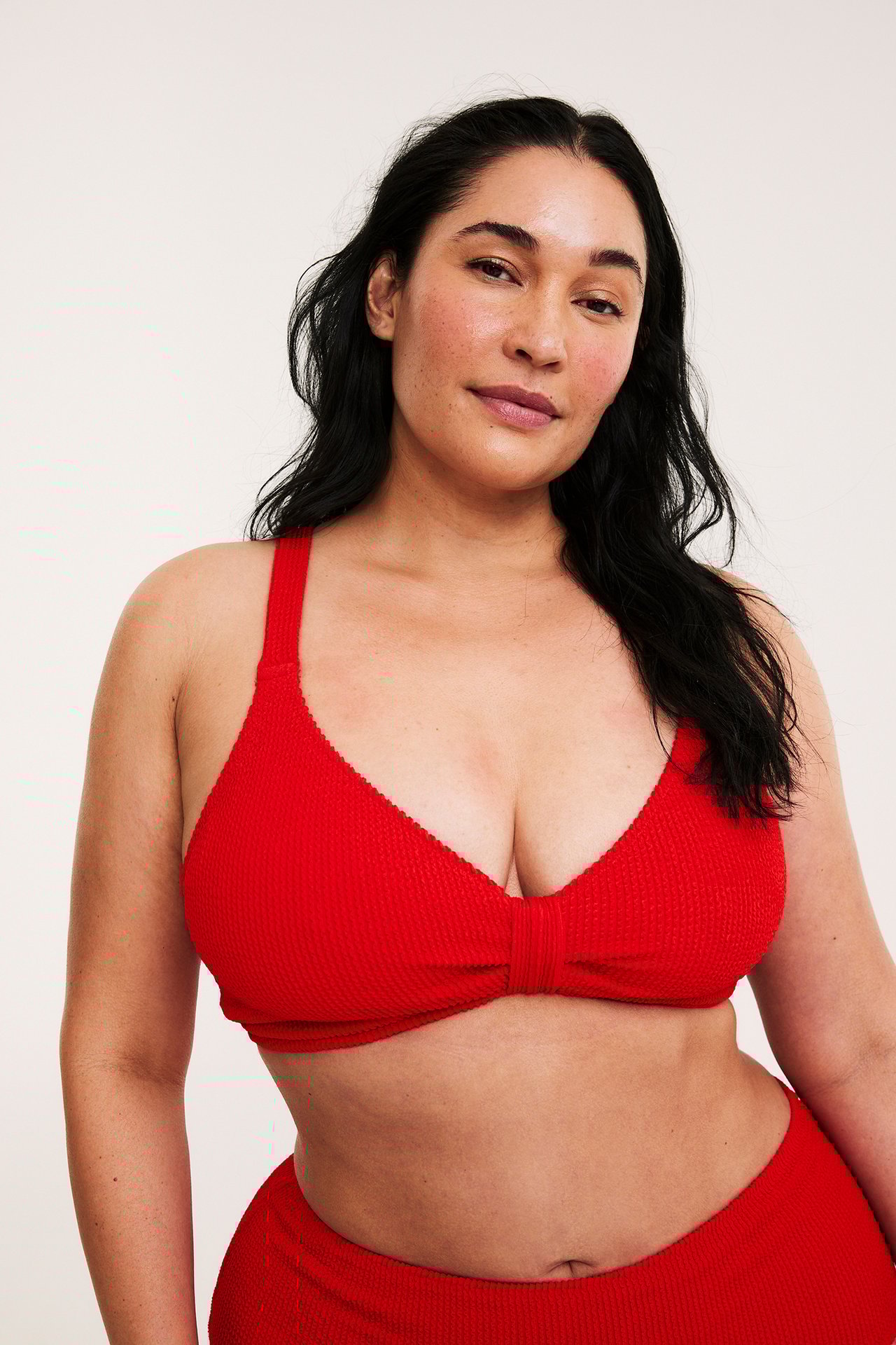 Frontvy: Kvinna bär en röd texturerad bikini-bh med justerbara band och matchande trosa.