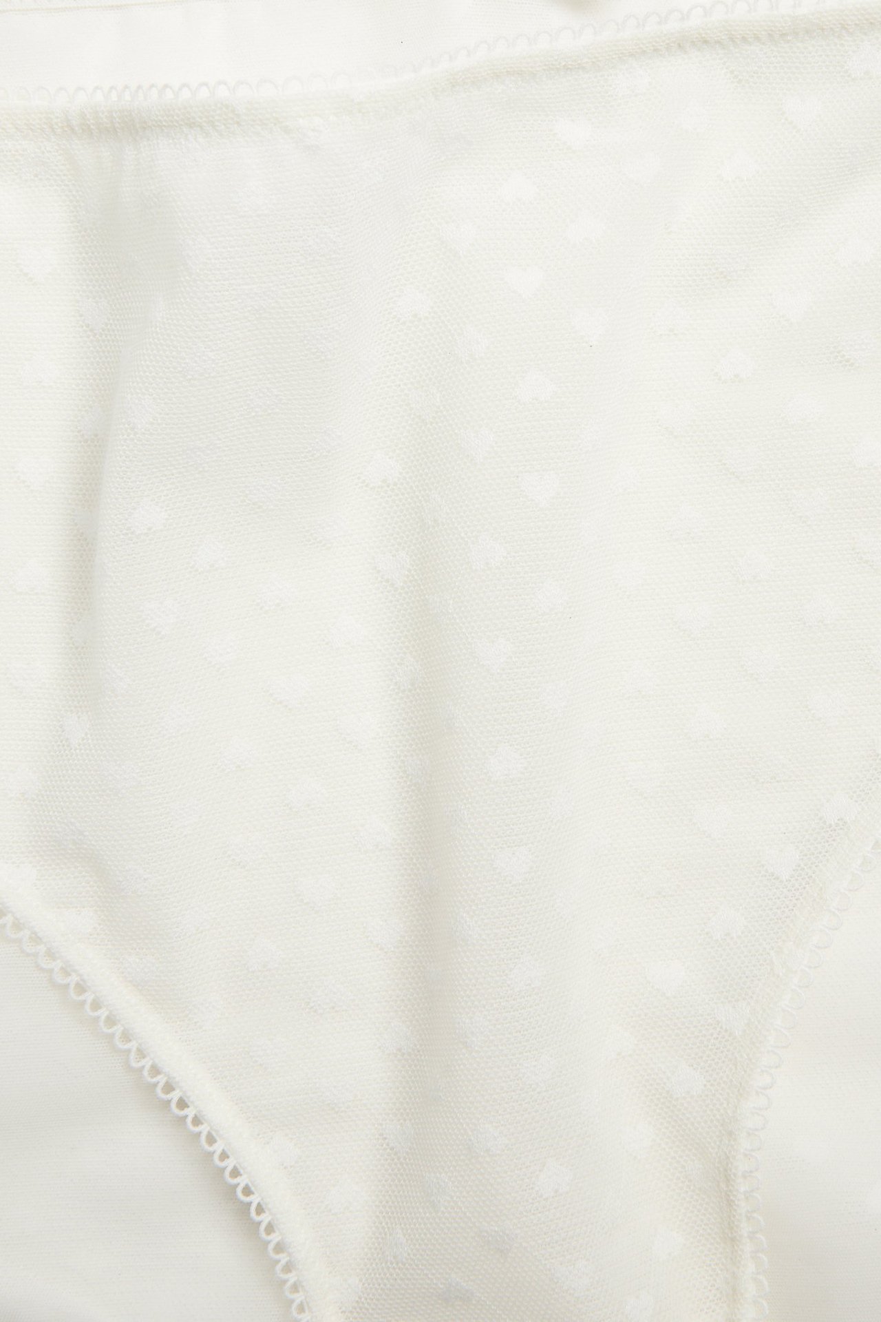 Nærbilde av offwhite mesh-brieftruse med diskret hjertemønster og delikat picotkant.