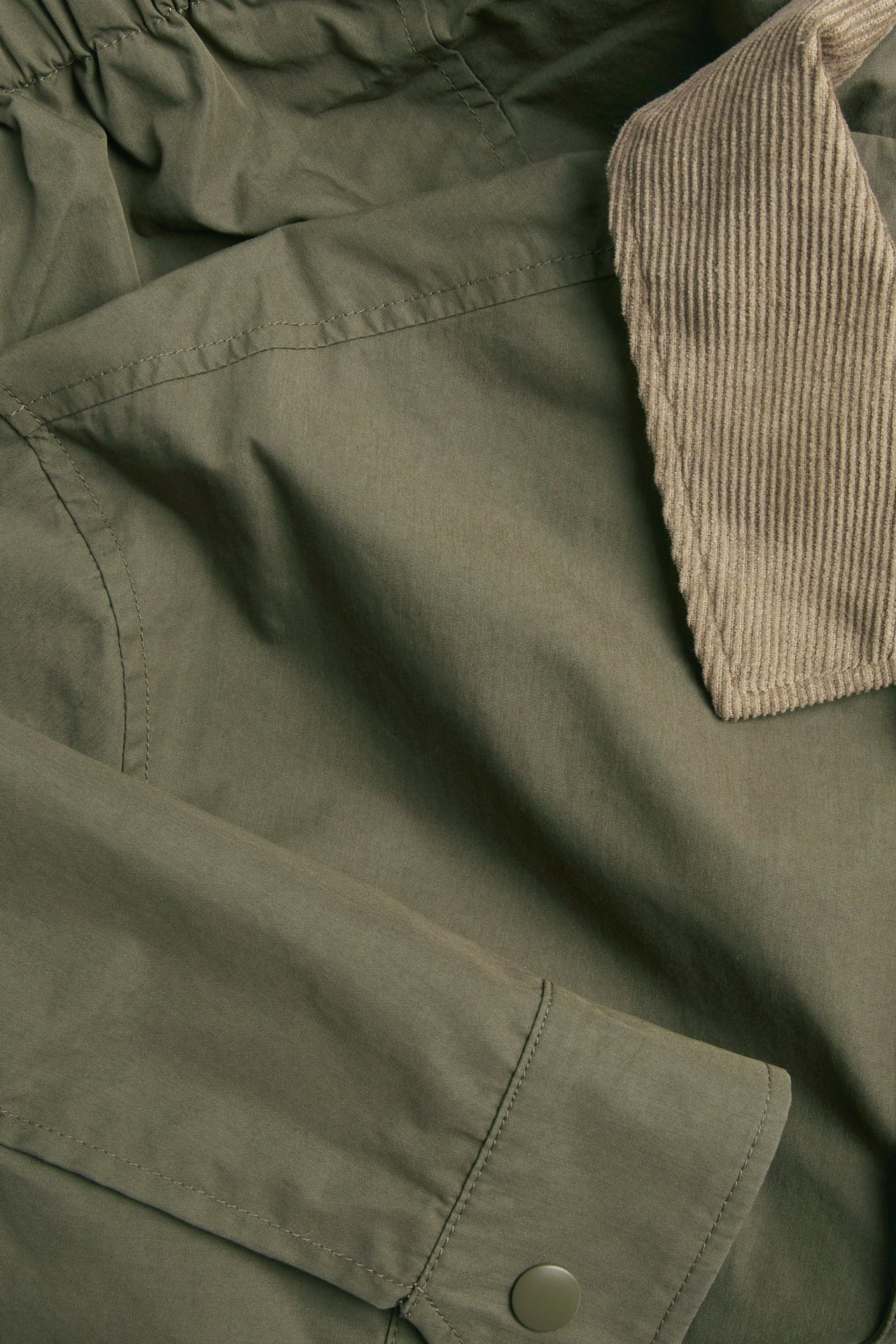 Zbliżenie męskiej zielonej kurtki z beżowym kołnierzem sztruksowym i zielonym guzikiem mankietu.