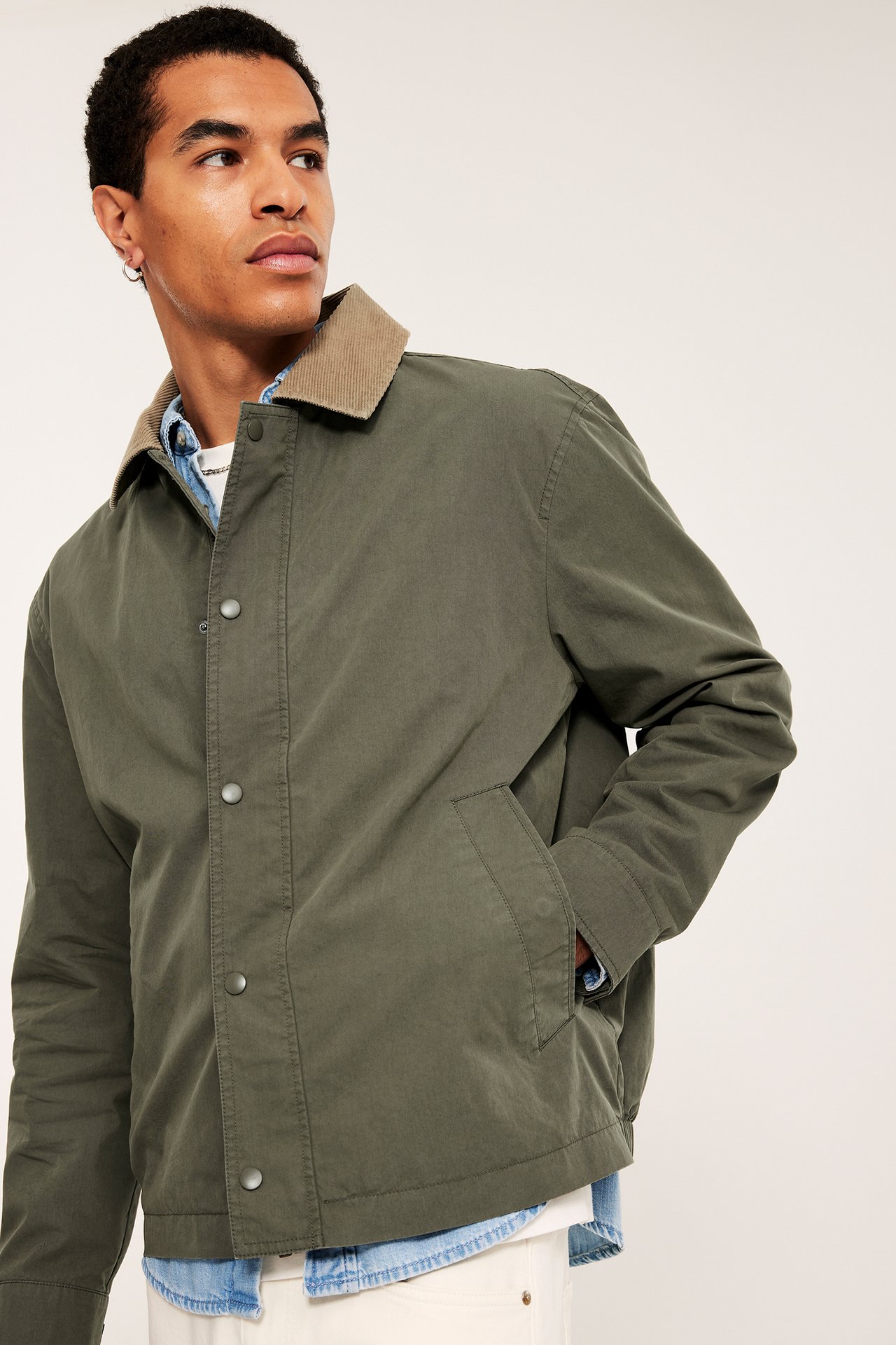 Frontutsikt av en mann i åpen grønn jakke med beige kordfløyelskrage over en dongeriskjorte.