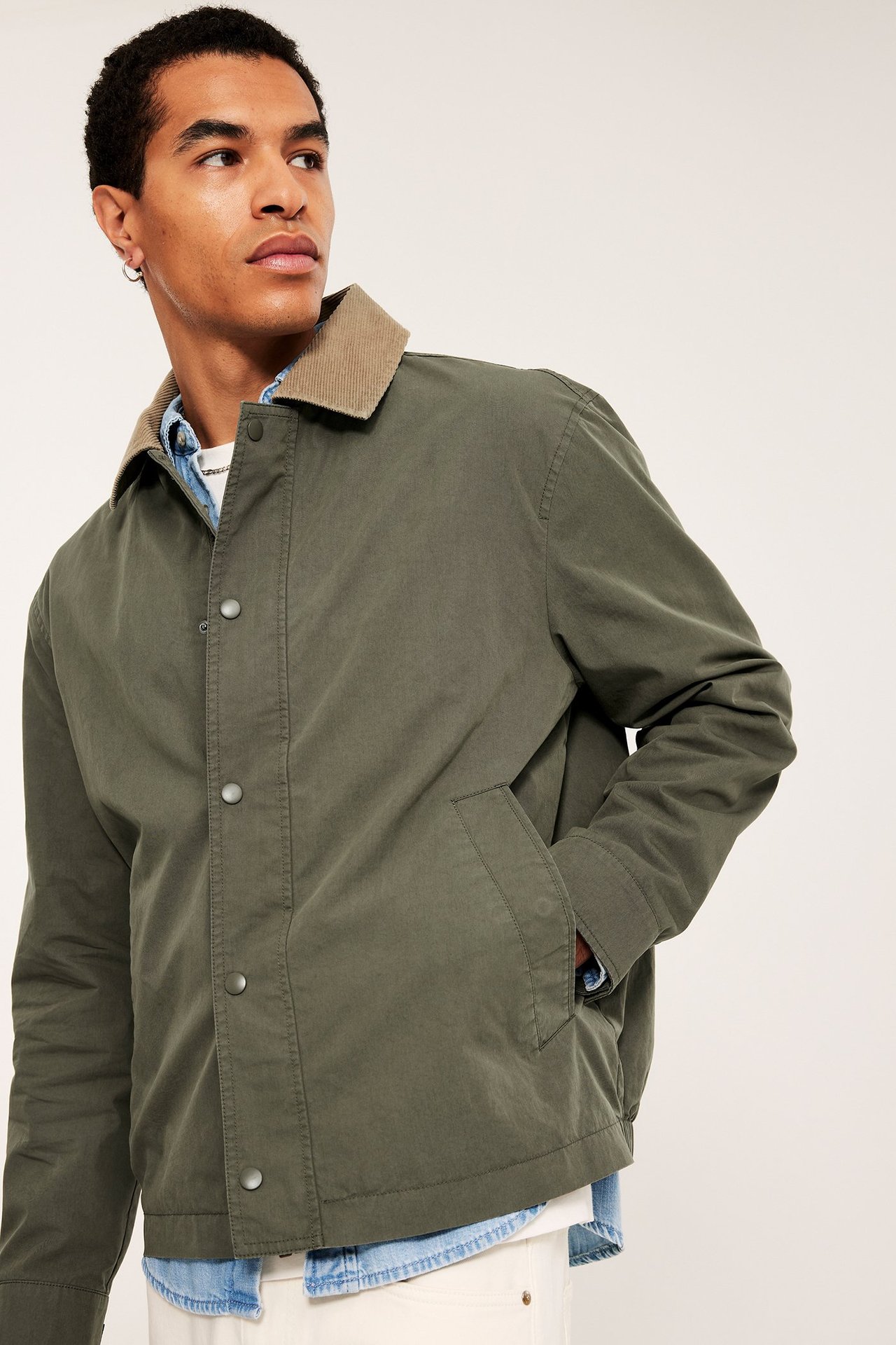 Widok z przodu mężczyzny w otwartej zielonej kurtce z beżowym kołnierzem sztruksowym na koszuli dżinsowej.