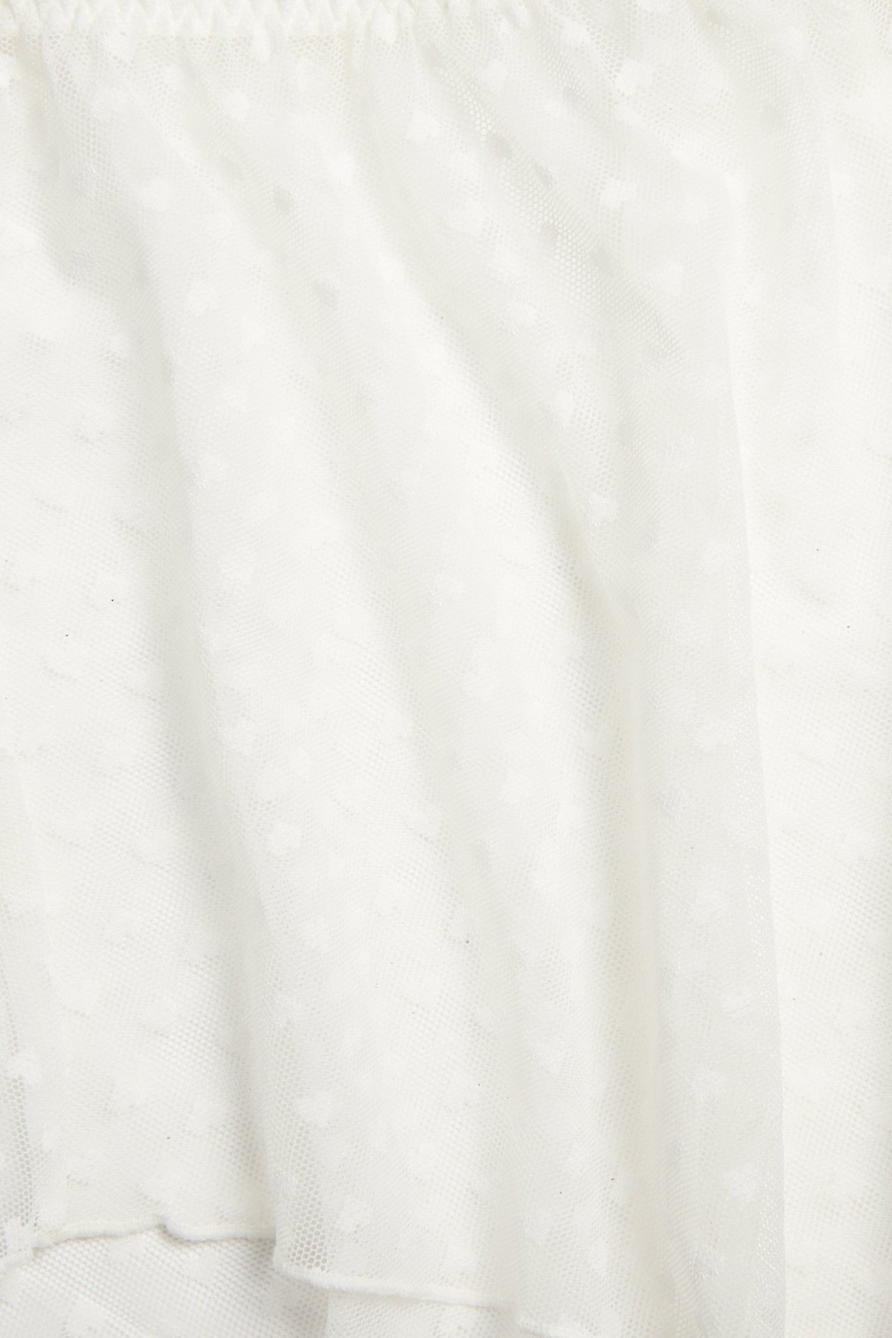 Nærbilde av offwhite gjennomsiktig meshshorts med subtilt hjertemønster og elastisk linning.