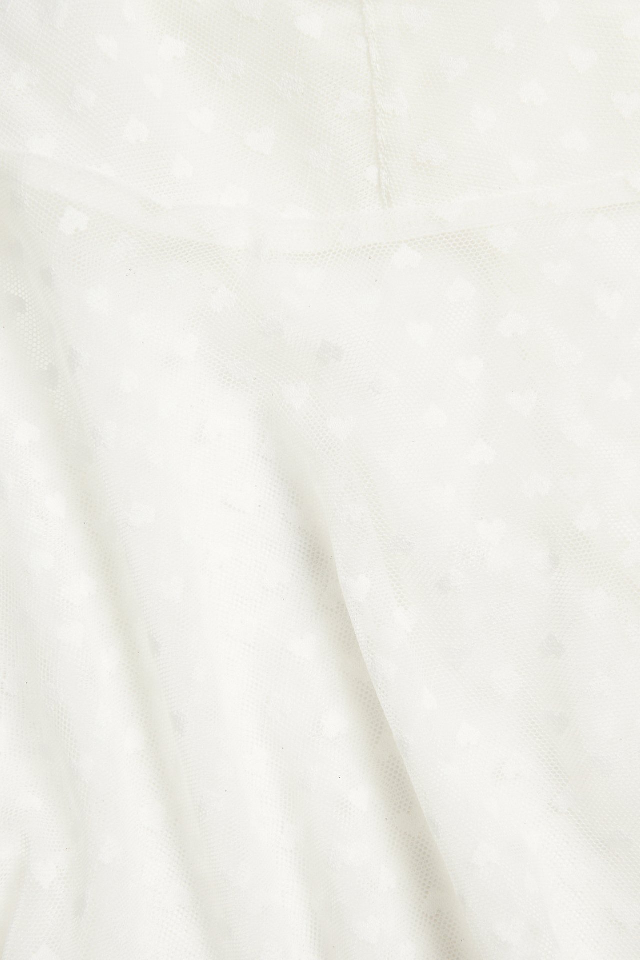 Närbild av ett offwhite meshlinne med subtilt hjärtmönster.