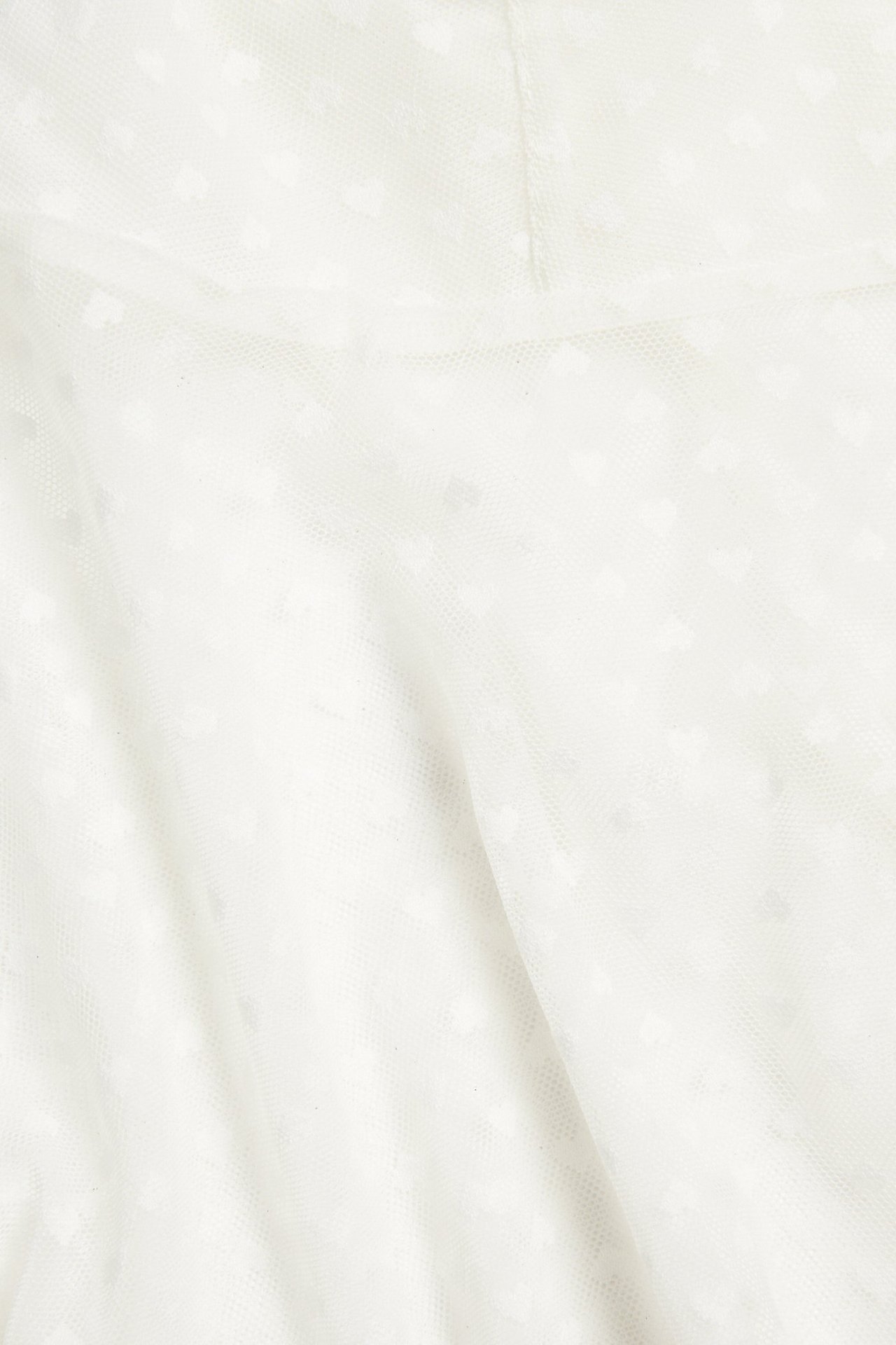 Närbild av ett offwhite meshlinne med subtilt hjärtmönster.