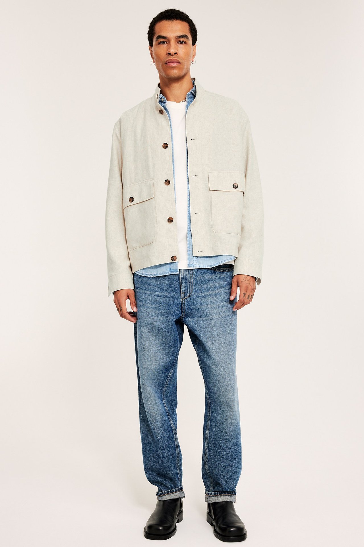 Edestä: Mies yllään vaalea pellavasekoitetakki valkoisen t-paidan, sinisten farkkujen ja mustien saappaiden kanssa.