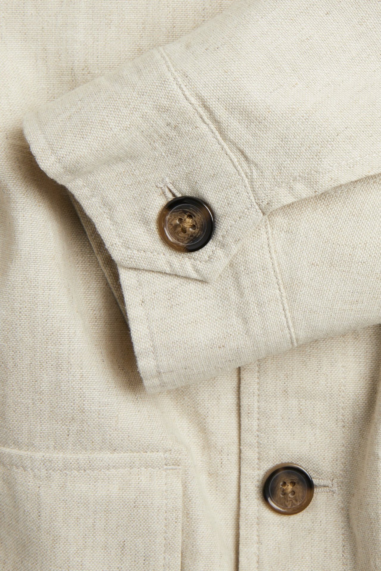 Lähikuva vaaleanbeigestä pellavasekoitetakista, näyttää hihansuun ruskealla napilla sekä taskun ja etunapin.