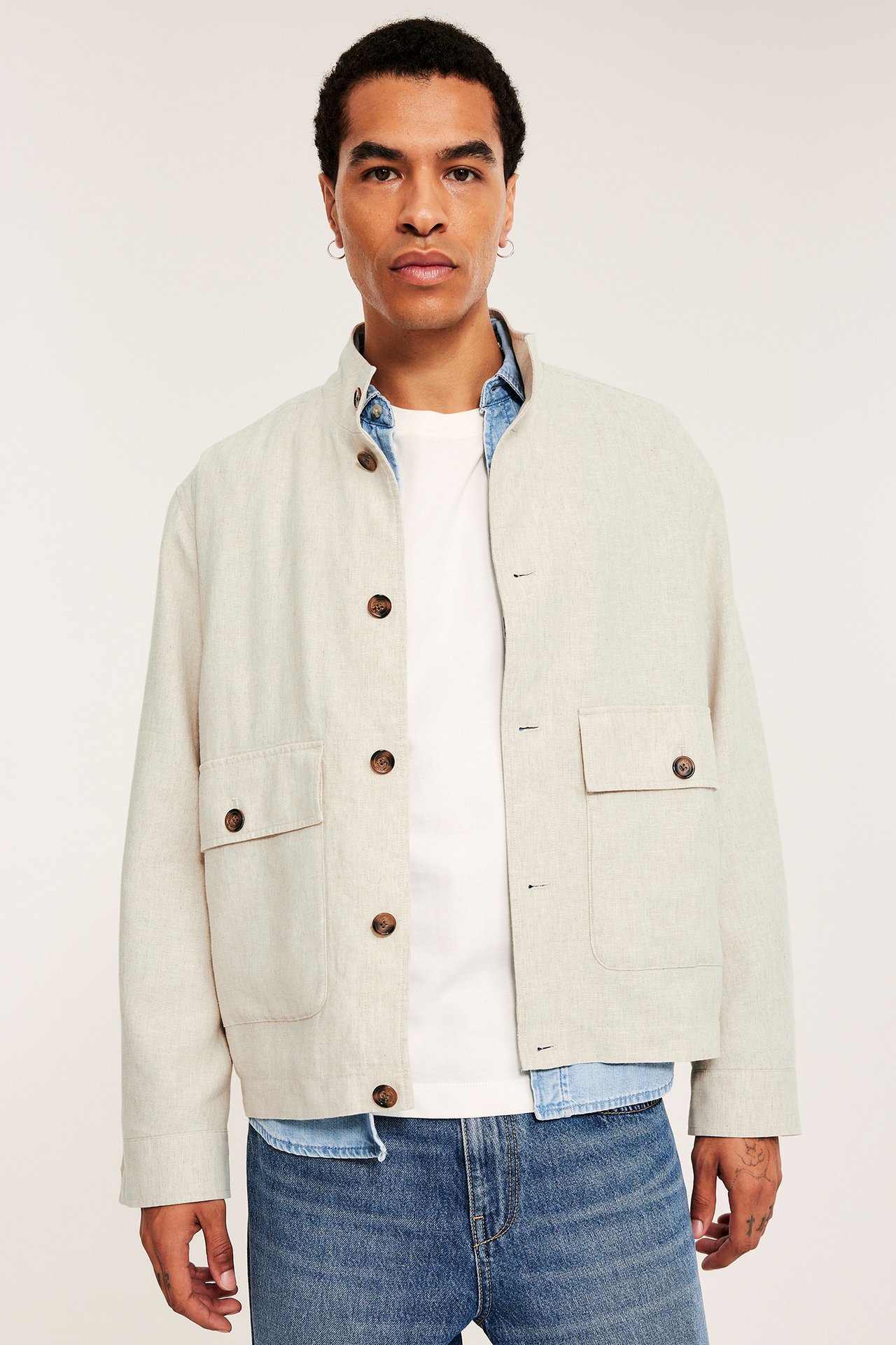 Frontvy: Man i ljusbeige jacka i linnemix med ståkrage och fickor, bärs över vit t-shirt och blå jeans.