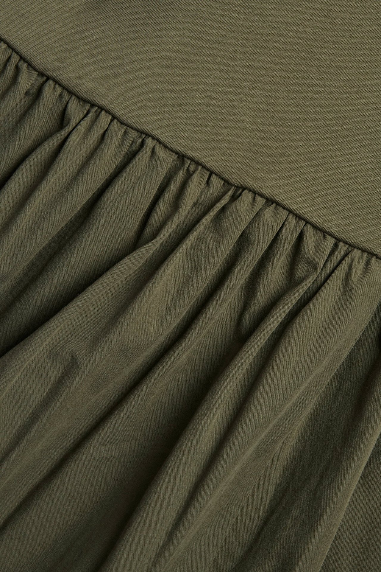 Zbliżenie zielonej sukienki z dzianinową górą i marszczoną spódnicą z popeliny.