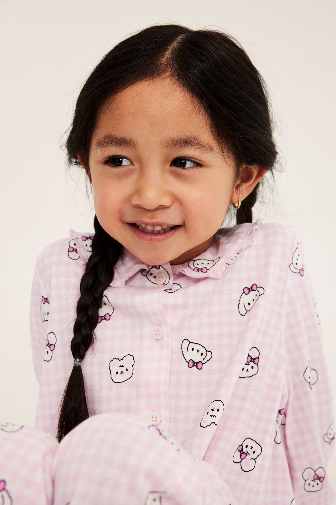 Lähikuva: lapsi yllään vaaleanpunainen ruudullinen puuvillapaita-pyjama eläinkuvioilla, röyhelökaulus.