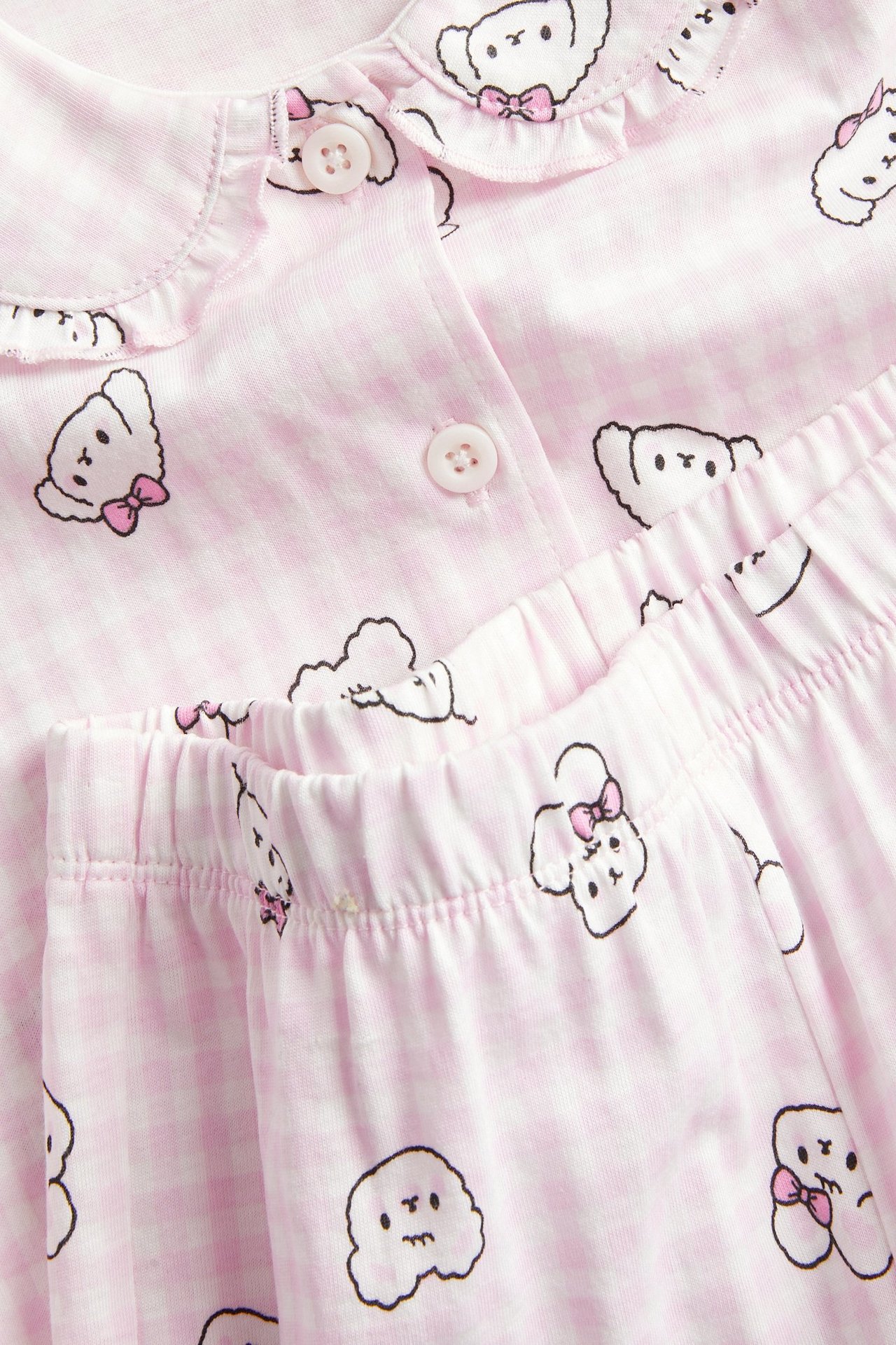 Zbliżenie na różową piżamę z dzianiny bawełnianej w kratkę vichy i wzór z kreskówkowymi psami.